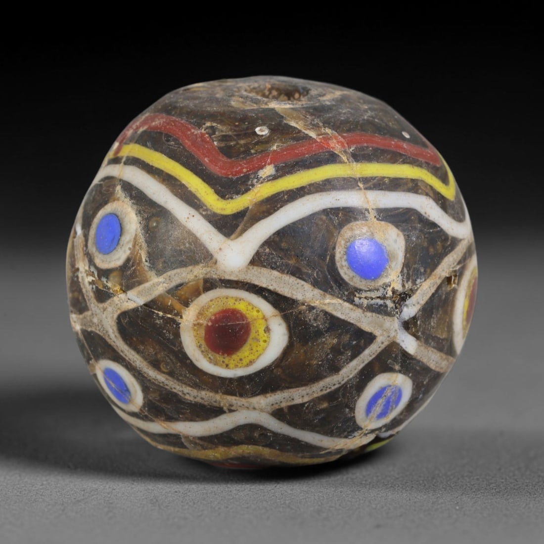 Ancient Canaanite & Phoenician Polychrome Eye Pattern Round Glass Bead (3000-300 BCE), 33AE: This antique polychrome round glass bead originates from Canaanite & Phoenician Cultures, the ancient Levantine maritime civilization famous for crafting protective eye motif glass talismans traded wi