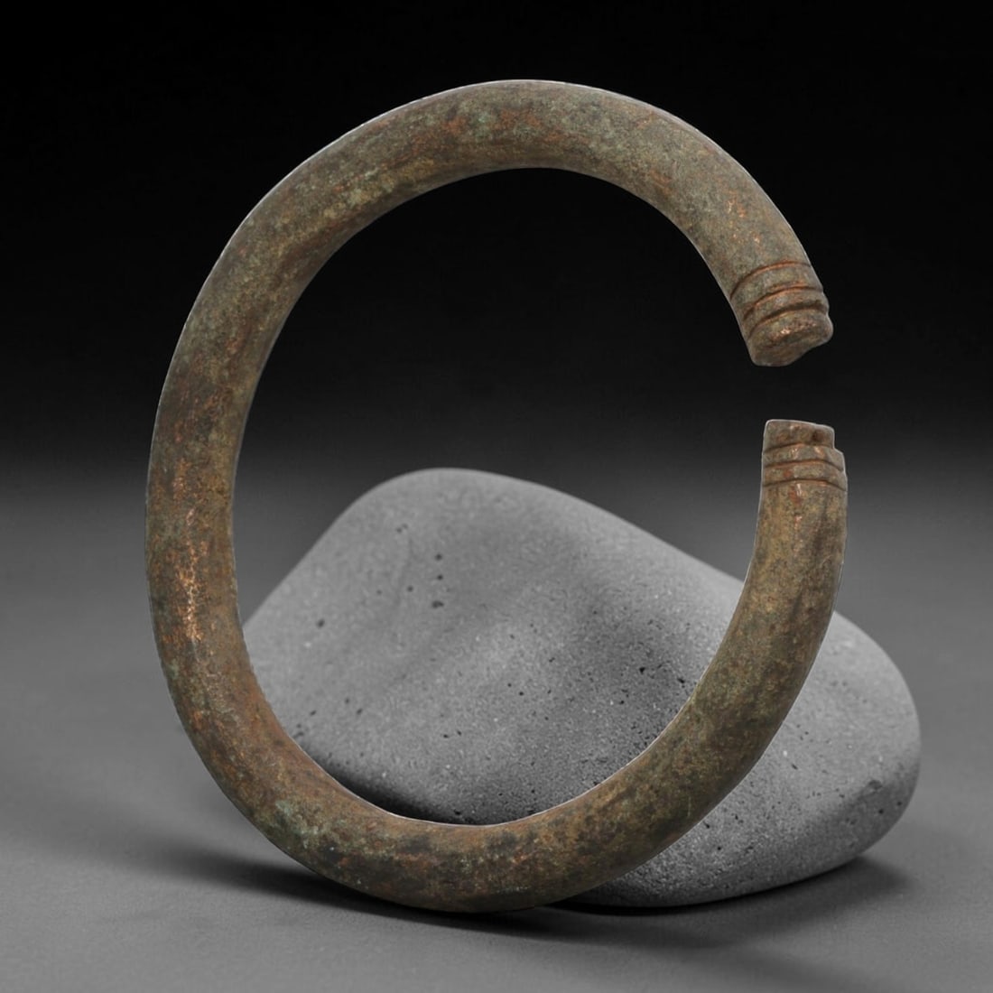 Ancient Bronze Bracelet - Roman Decorated Penannular Bangle, 88BN: A penannular bronze bracelet of ancient Roman origin, formed from a thick, rounded bronze band. The open terminals are adorned with raised collars, a simple decorative motif common in Roman provincial