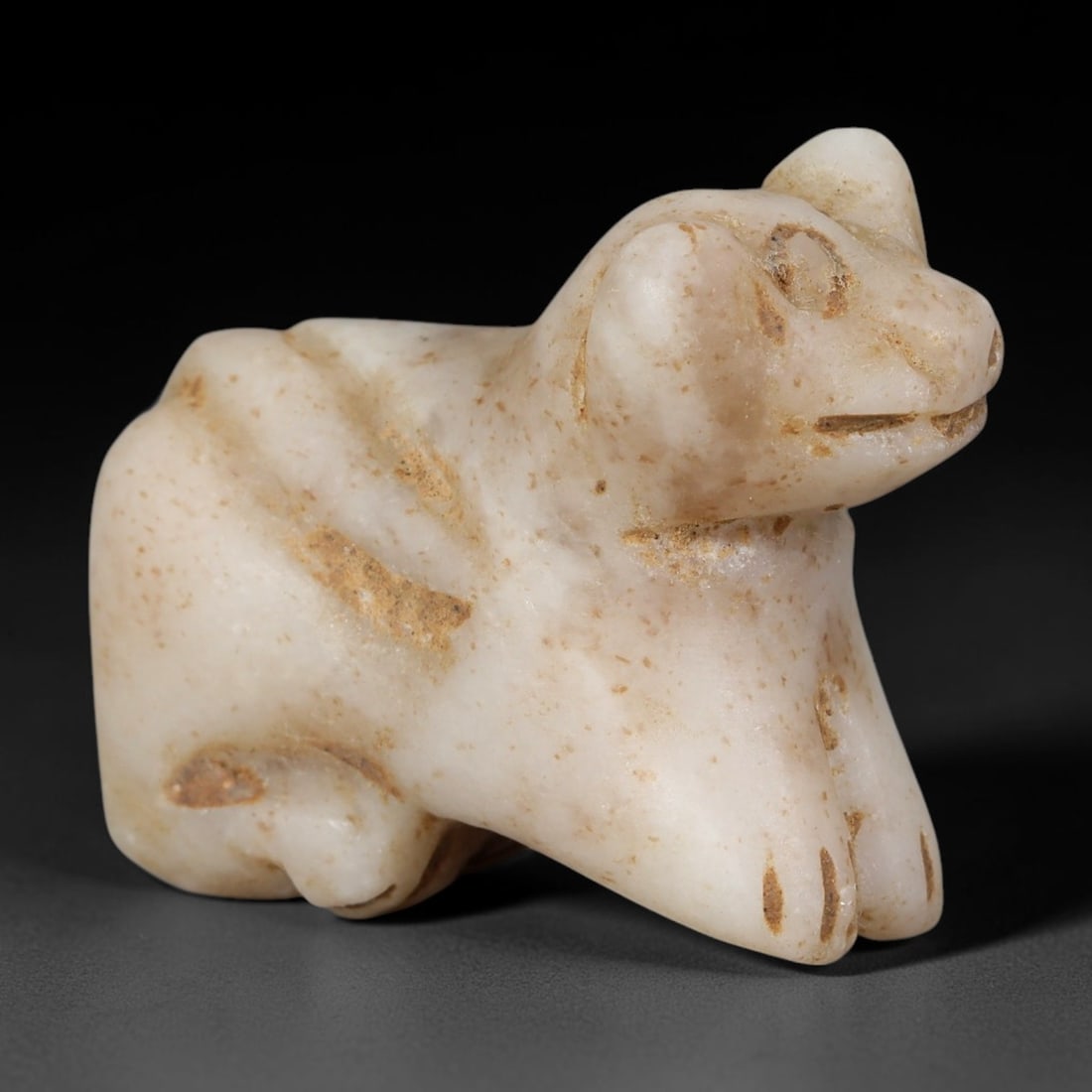 Ancient Near Eastern White Calcite Recumbent Bull Amulet (800-300 BCE), 41AB: Miniature hand-carved pale creamy white calcite talisman depicting a resting bull with stylised simplified facial carving for eyes, mouth and hooves. Natural warm amber speckled burial staining permea