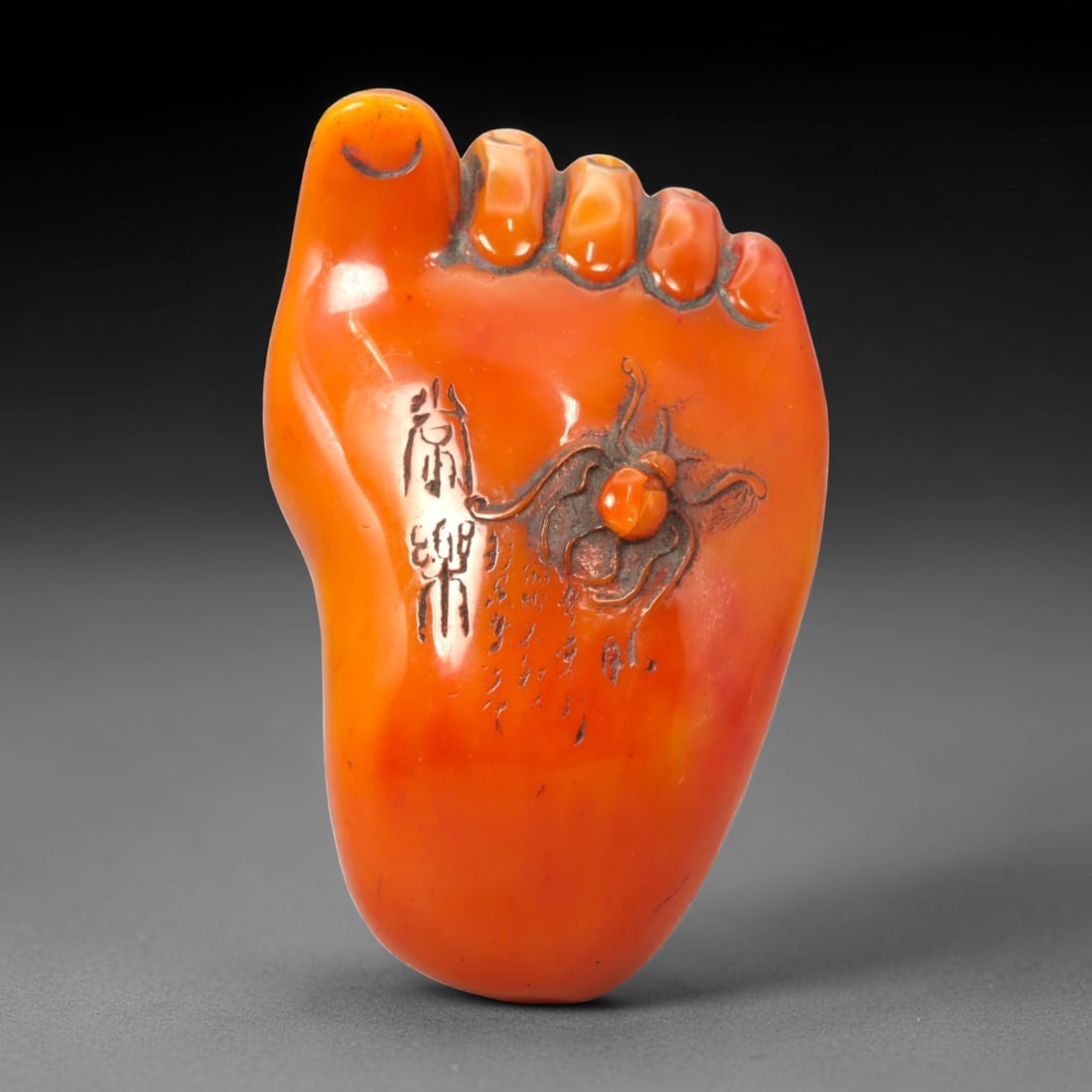 A Chinese Amber-Resin Foot-Form Carving, 64FC: Modeled from translucent orange-toned amber resin, the object is carved in the form of a stylized human foot, rendered in the round with simplified anatomical features. The toes are indicated in shall