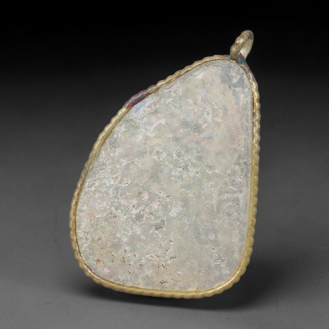 Ancient Roman Glass Slag in Modern Gilt-Edge Pendant, 38EH: This contemporary pendant is crafted from ancient Roman glass slag, featuring a fragmented, iridescent glass surface with weathered patina. The irregular form is bordered by a subtle gilt frame, added