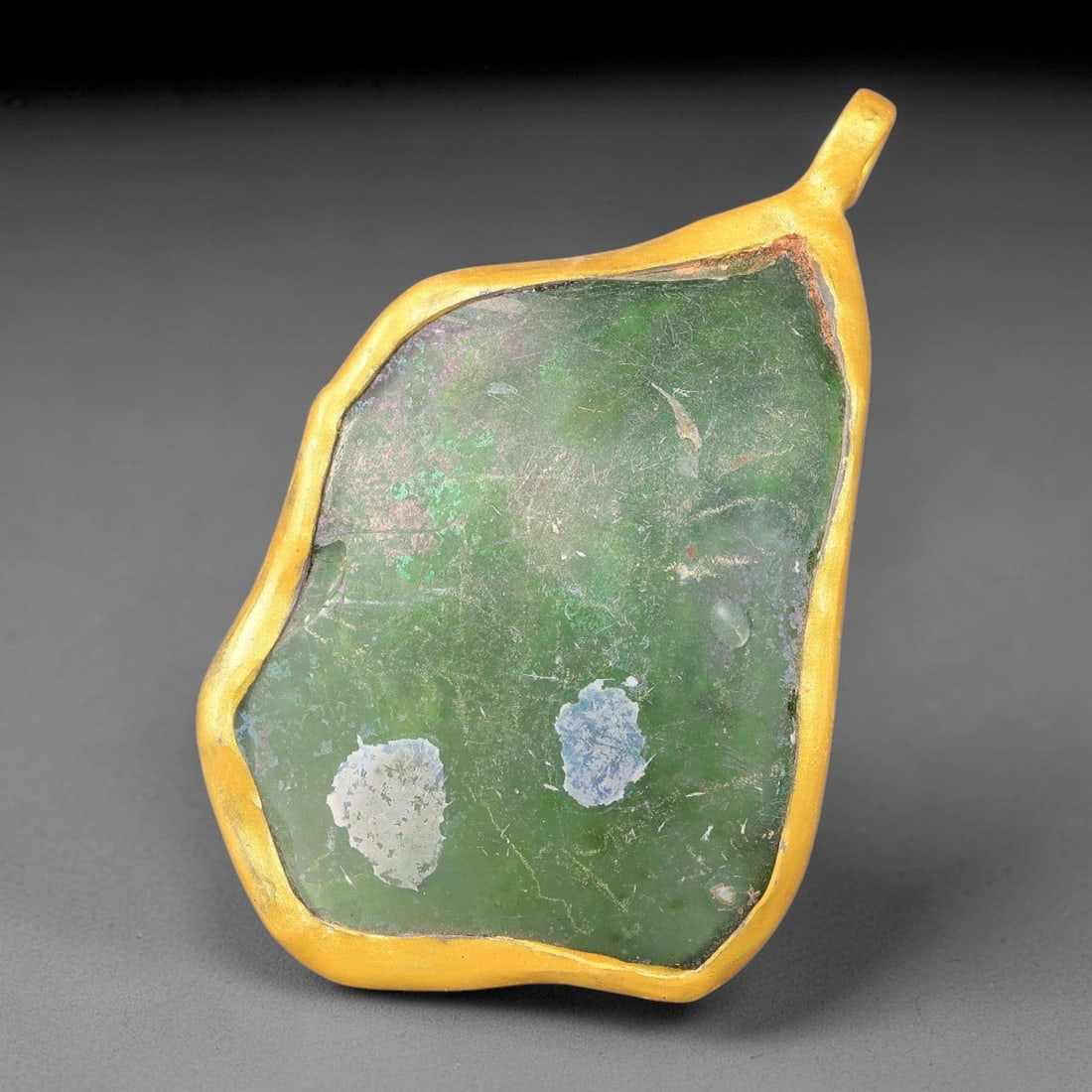 Ancient Roman Glass Slag in Modern Gilt-Edge Pendant, 52FY: This contemporary pendant is crafted from ancient Roman glass slag, featuring a fragmented, iridescent glass surface with weathered patina. The irregular form is bordered by a subtle gilt frame, added