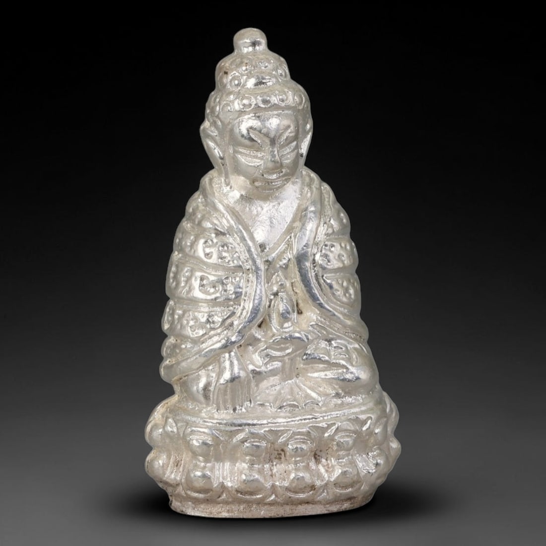 Thai Silvered Metal Mini Sacred Statuette Amulet, 4AH: Compact cast metal sacred figurine with silvered finish, featuring detailed embossed relief patterns covering the robe, head ornamentation and tiered pedestal base. Minor natural wear and faint patina