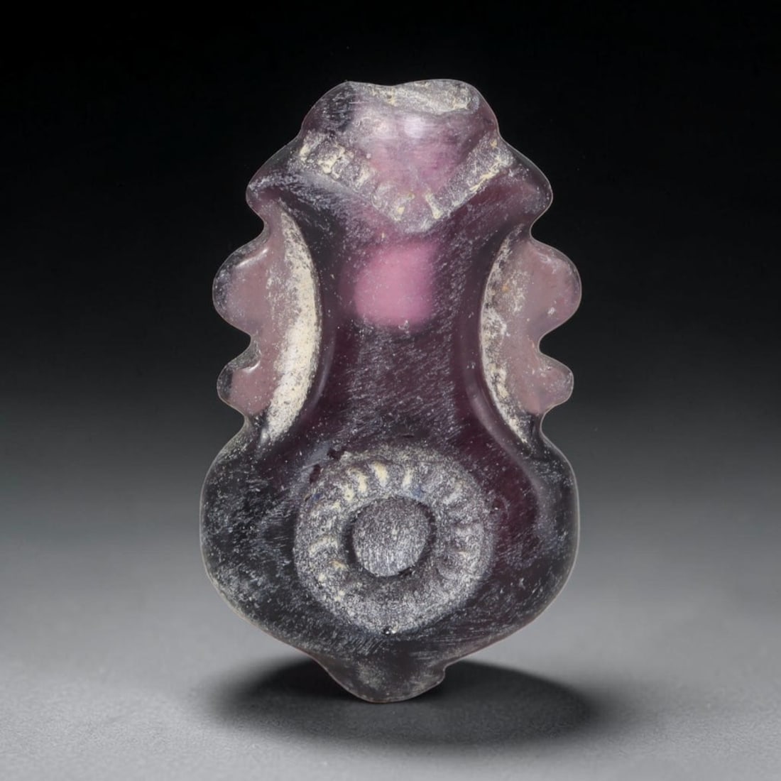 Ancient Medieval Amethyst Vase Shaped Bead, 70EQ: This ornamental pendant bead is carved from natural amethyst dating to the Medieval period, formed in an elegant vase silhouette with symmetrical flanking decorative contours and central circular moti