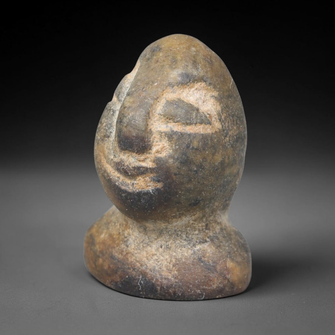 Ancient Bactrian Composite Stone Idol Head (c.2300-1700 BCE), 7ER: This miniature carved idol head originates from ancient Bactrian cultural traditions, worked from composite stone with simplified incised facial features and a stable pedestal base, typical stylistic 