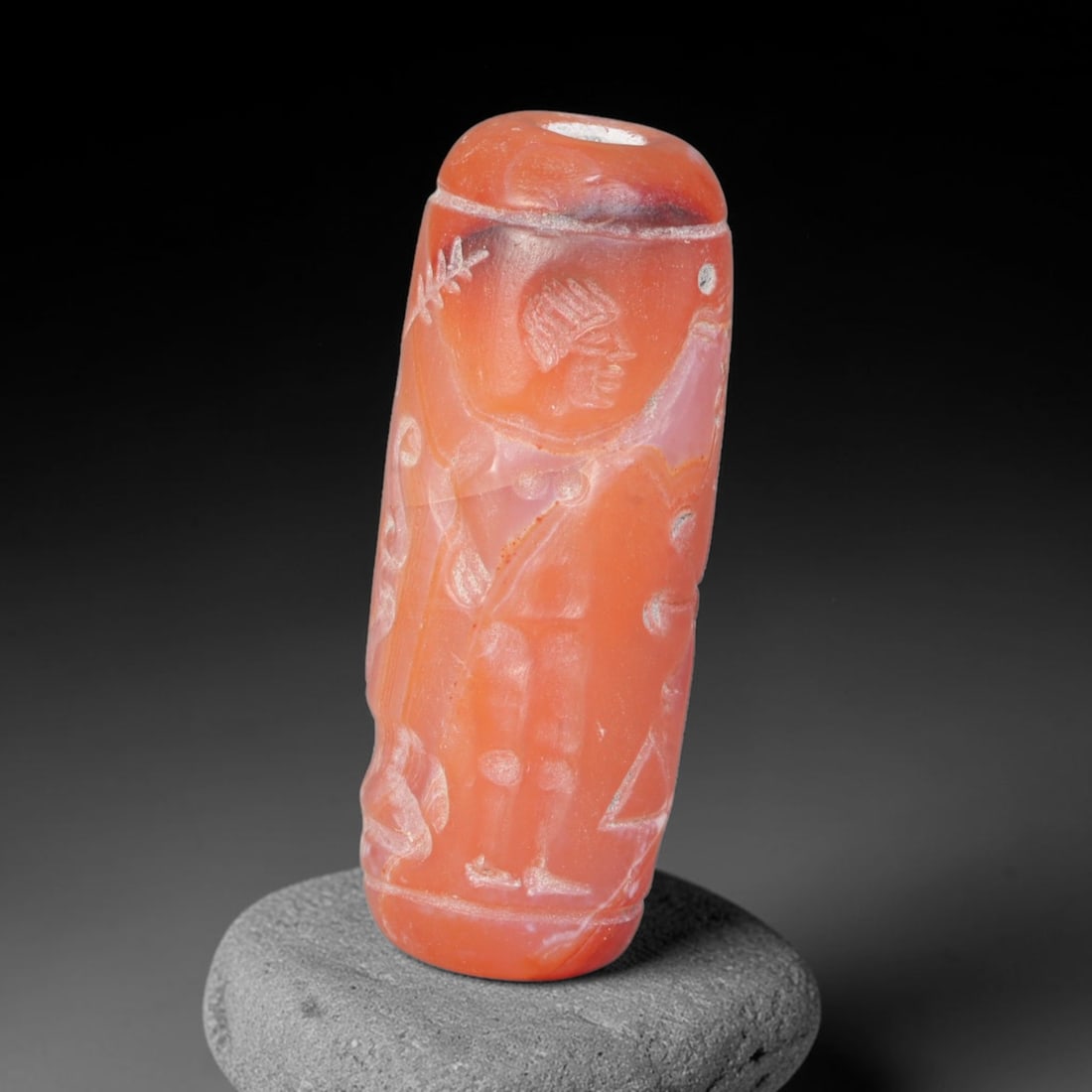 Ancient Achaemenid Persian Carnelian Cylinder Seal (550-330 BCE), 88EQ: This cylindrical seal is carved from warm translucent carnelian originating from the Achaemenid Persian cultural sphere, engraved with a scene featuring a standing human figure confronting a horned be