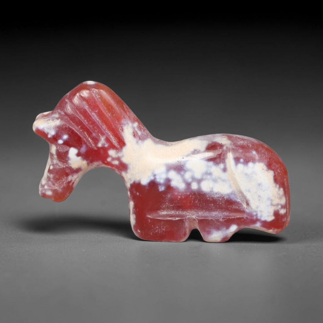 Ancient Bactrian Banded Agate Horse Effigy Amulet (c.200-200 BCE), 64EQ: Hand-carved from rich red-and-white mottled banded agate originating from ancient Bactria of Central Asia. Modelled as a stylised recumbent horse talisman with simplified streamlined proportions typic
