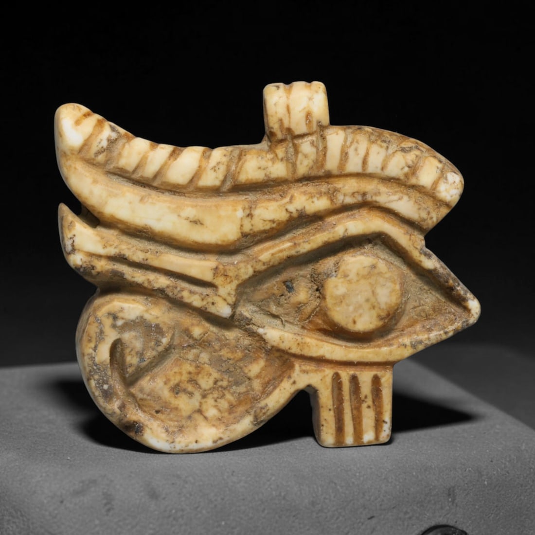 Ancient Pharaonic Egyptian Wedjat Eye Amulet (4000 BCE-30 CE), 30ED: This carved pale stone Wedjat Eye amulet originates from Pharaonic Egyptian Civilization, the revered emblem of protection, wellness and spiritual wholeness in ancient Egyptian belief. The amulet disp
