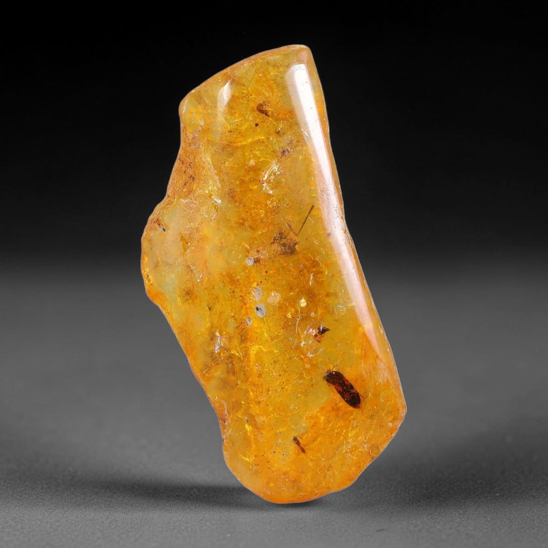 10.95ct Natural Baltic Polished Loose Freeform Amber Gemstone, 80FL: This smoothly polished freeform amber piece carries warm translucent organic clarity with fine natural fossil flecks and tiny mineral inclusions suspended throughout its 32x15x8mm flowing unstructured