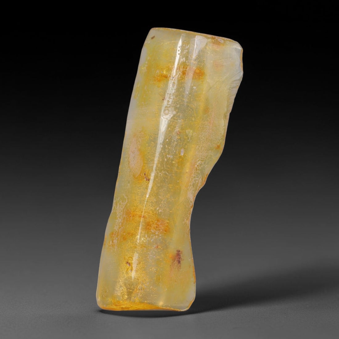 18.18ct Natural Baltic Polished Loose Freeform Amber Gemstone, 26AT: This smoothly polished freeform amber piece carries warm translucent organic clarity with fine natural fossil flecks and tiny mineral inclusions suspended throughout its 49x18mm flowing unstructured s