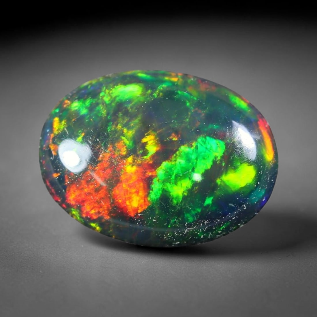 1.73ct Natural Ethiopian Welo Black Smoked Opal Cabochon Loose Gemstone, 15FX: This fully polished Ethiopian Welo opal features a dark smoked base with vivid, sweeping play-of-color shifting across its glossy dome surface, measured at 11x8x3mm. The black smoke treatment deepens 