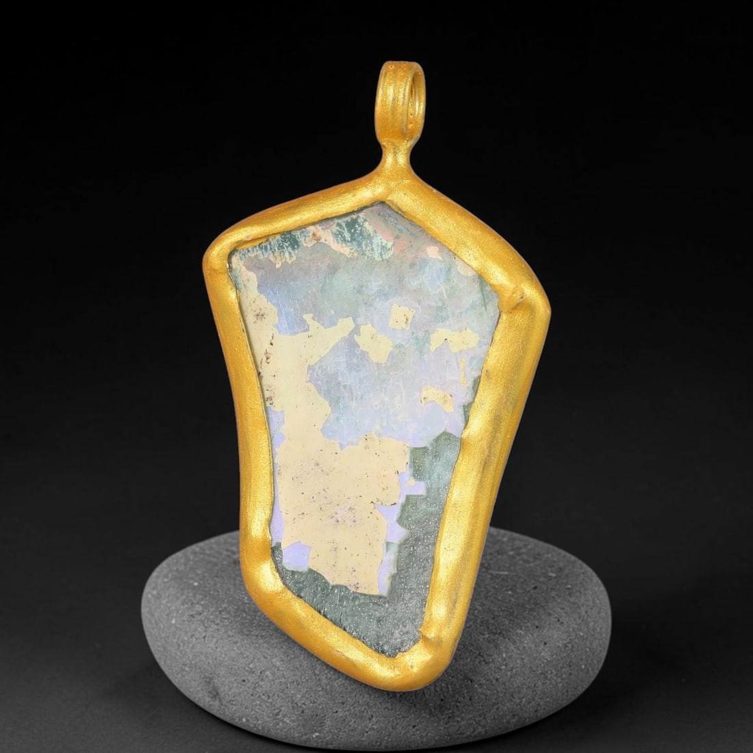 Ancient Roman Glass Slag in Modern Gilt-Edge Pendant, 64FY: This contemporary pendant is crafted from ancient Roman glass slag, featuring a fragmented, iridescent glass surface with weathered patina. The irregular form is bordered by a subtle gilt frame, added