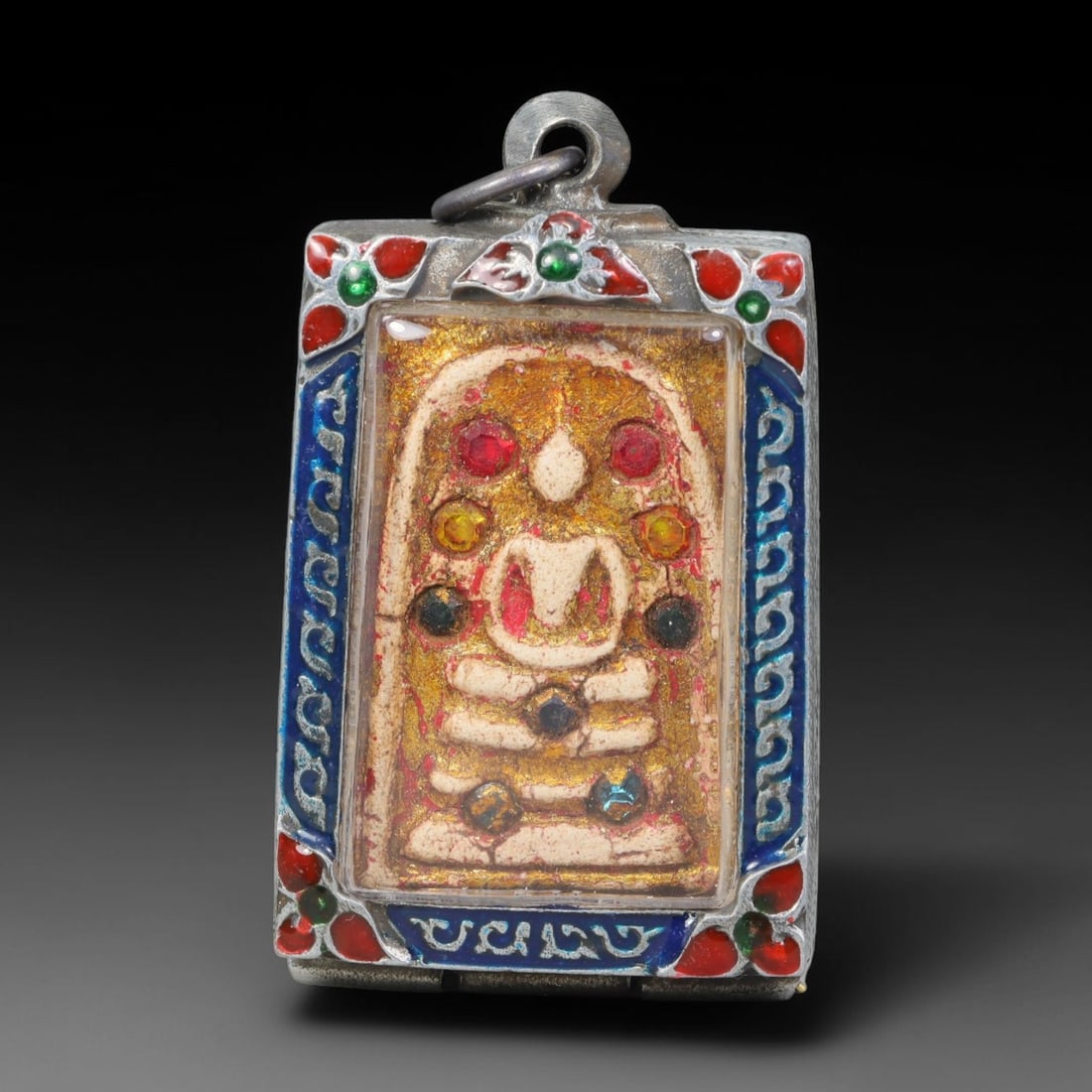 Thai Buddhist Folk Tradition Enclosed Amulet Pendant with Decorative Metal Casing, 20AH: This Thai sacred amulet is housed within an ornate hinged metal protective casing fitted with a top loop for wear as a pendant. The casing features intricate embossed surface detailing and a continuou