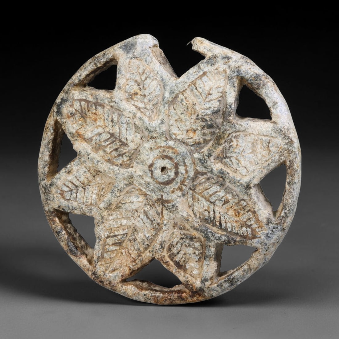 Ancient Neo-Hittite Openwork Circular Stone Stamp Seal (1200-800 BCE), 28EF: This circular openwork stamp seal is carved from weathered stone, originating from Iron Age Neo-Hittite cultures of Northern Syria and Eastern Anatolia. The seal face displays an intricate pierced ros