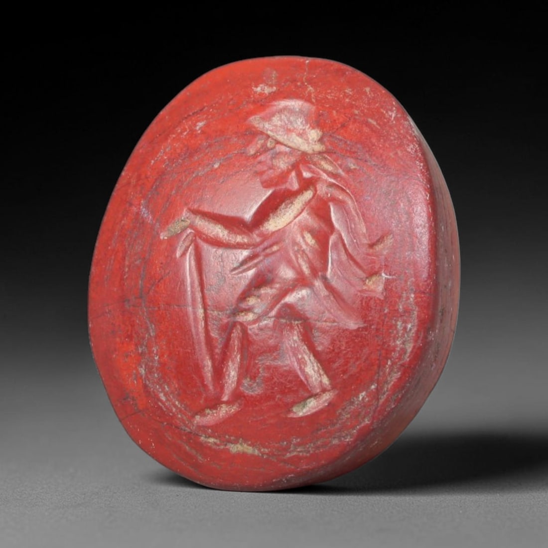 Ancient Roman Imperial Red Jasper Intaglio Bead (1st Century BCE - 3rd Century CE), 72EQ: This antique bead is carved from rich red jasper, fashioned as a wearable intaglio seal originating from the Roman Imperial sphere. The face bears an engraved walking robed traveller figure with cap, 