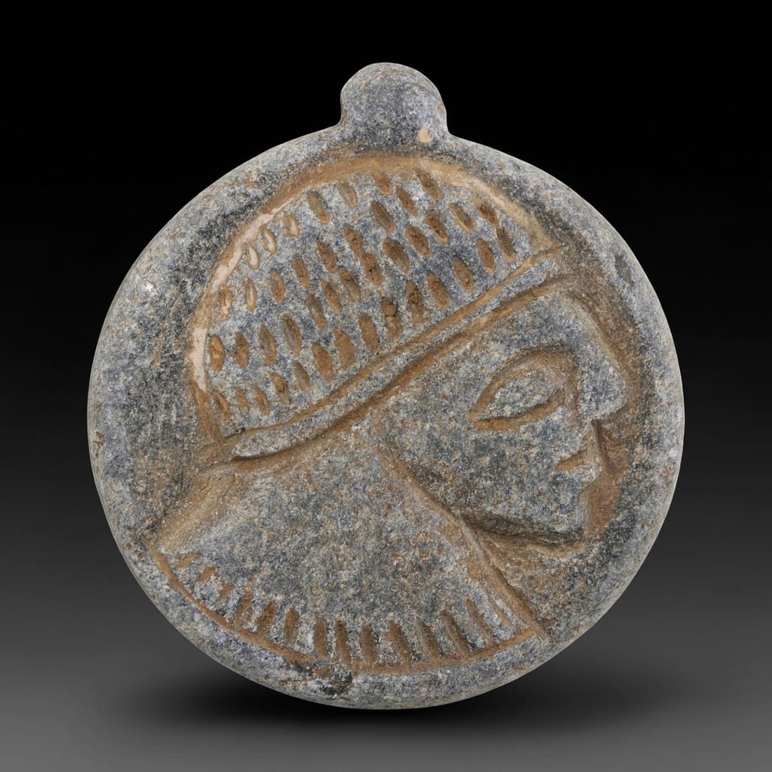 Antique Medieval Islamic Carved Stone Amulet with Profile Head Motif, 91AN: Crafted from weathered grey stone with earthy patina, this circular amulet features a deeply incised profile of a human head, characteristic of medieval Islamic decorative traditions. The figure wears