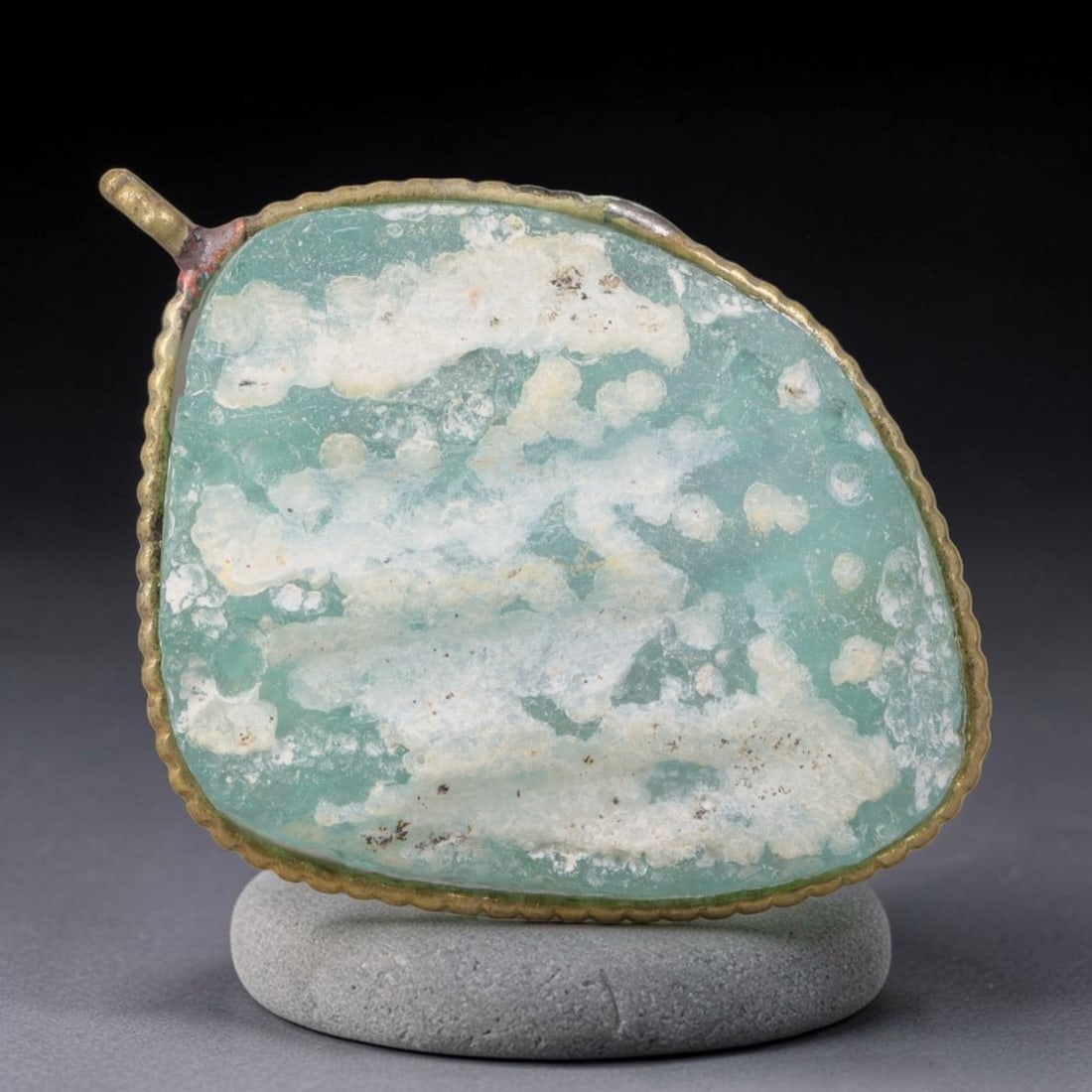 Ancient Roman Glass Slag in Modern Gilt-Edge Pendant, 24EH: This contemporary pendant is crafted from ancient Roman glass slag, featuring a fragmented, iridescent glass surface with weathered patina. The irregular form is bordered by a subtle gilt frame, added