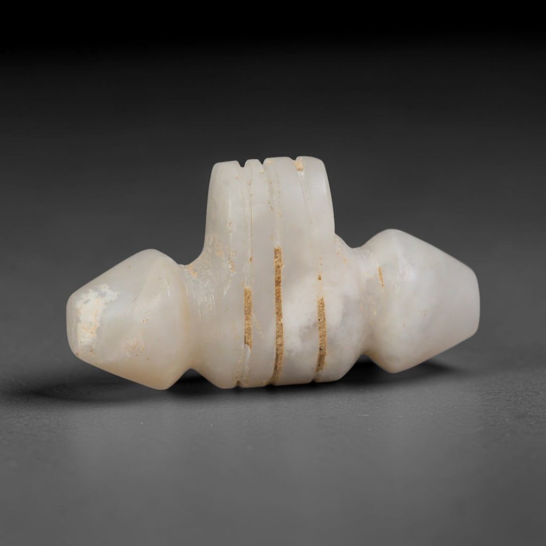 Ancient Sasanian Persian Carved Stone Amulet (c.224-651 CE), 91ED: This pale translucent stone amulet originates from Ancient Sasanian Persian culture. The symmetrical stylised form features segmented incised grooves along its central body, shaped with tapered termin