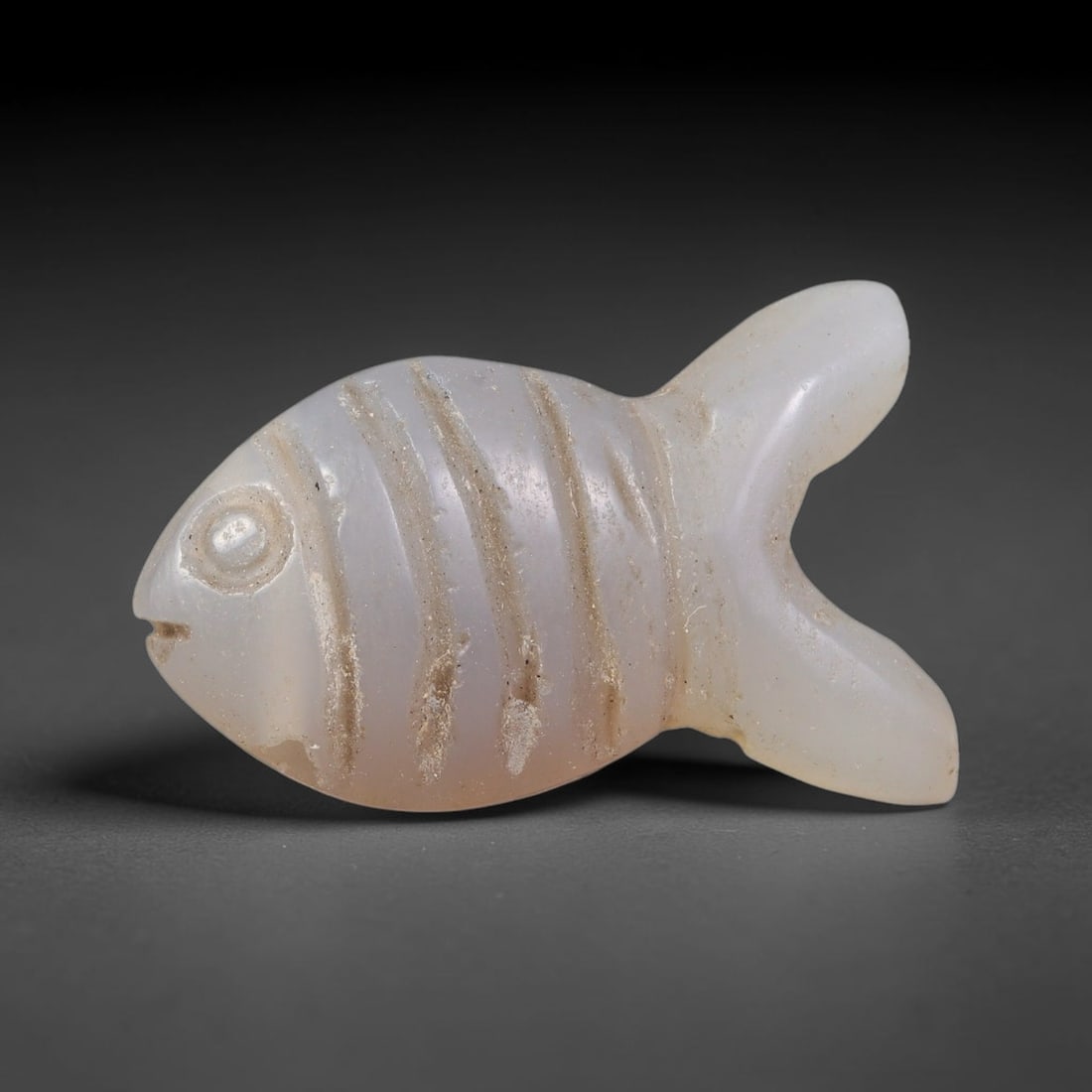 Ancient Coptic Christian Egyptian Culture Chalcedony Fish Amulet Bead (300-1000 CE), 37EC: This antique fish-shaped amulet bead carved from pale chalcedony originates from Coptic Christian Egyptian culture, where the fish served as a core sacred symbol of faith and protection within early C