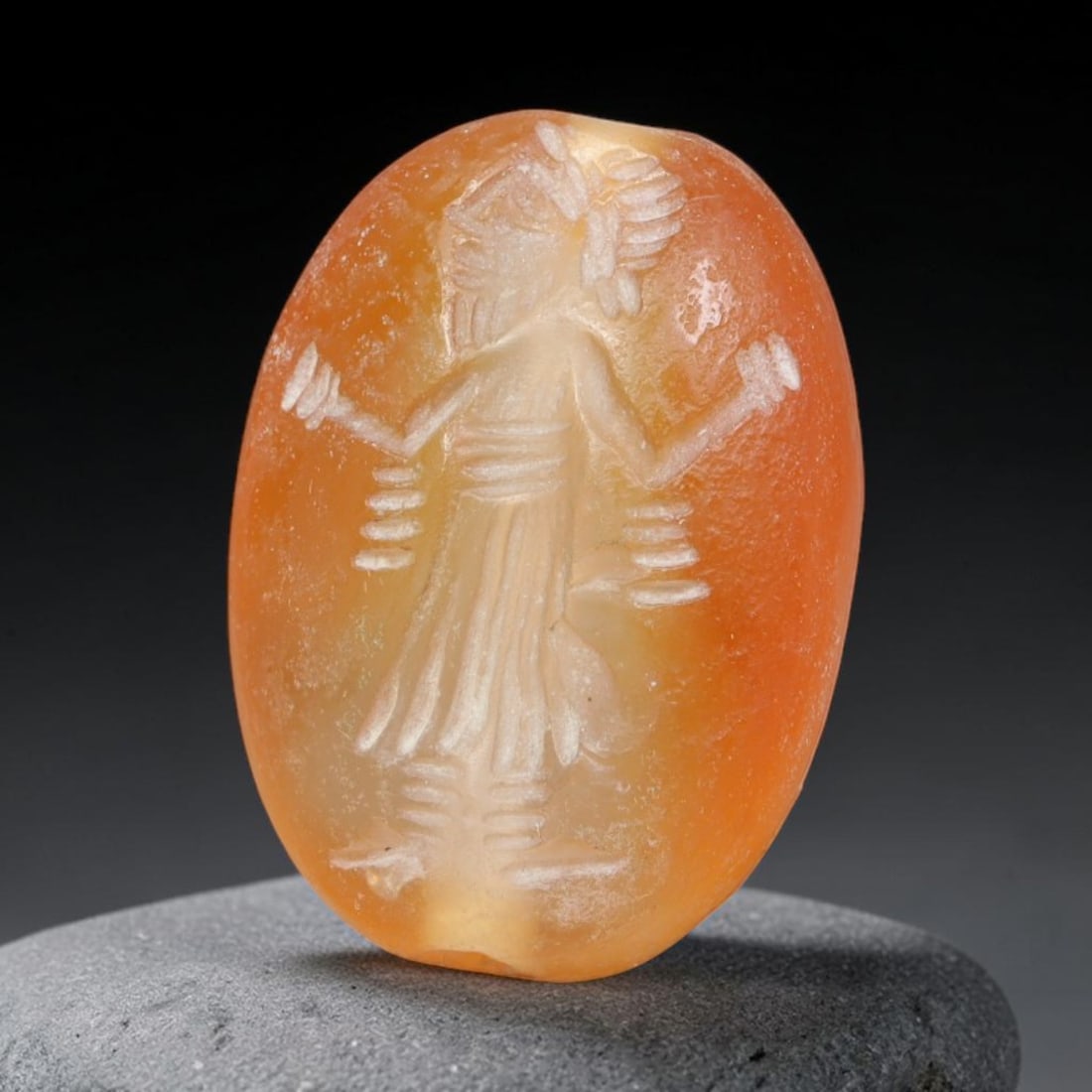 Ancient Sasanian Persian Carnelian Intaglio Bead (224-651 CE), 62EQ: This antique wearable seal bead is crafted from warm translucent carnelian originating from the Sasanian Persian Empire, bearing an intaglio carving of a standing robed figure adorned with stylized ar