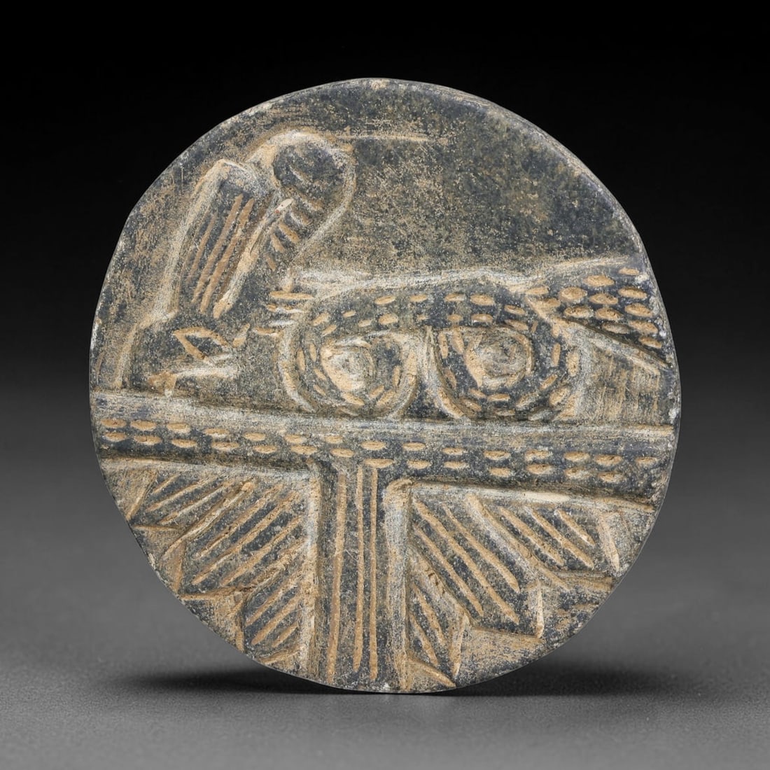 Ancient Neo-Hittite Dark Stone Relief Plaque (1200-800 BCE), 38EF: This circular relief plaque is carved from dark metamorphic stone, originating from Iron Age Neo-Hittite cultures of Northern Syria and Eastern Anatolia. The surface bears finely incised relief iconog