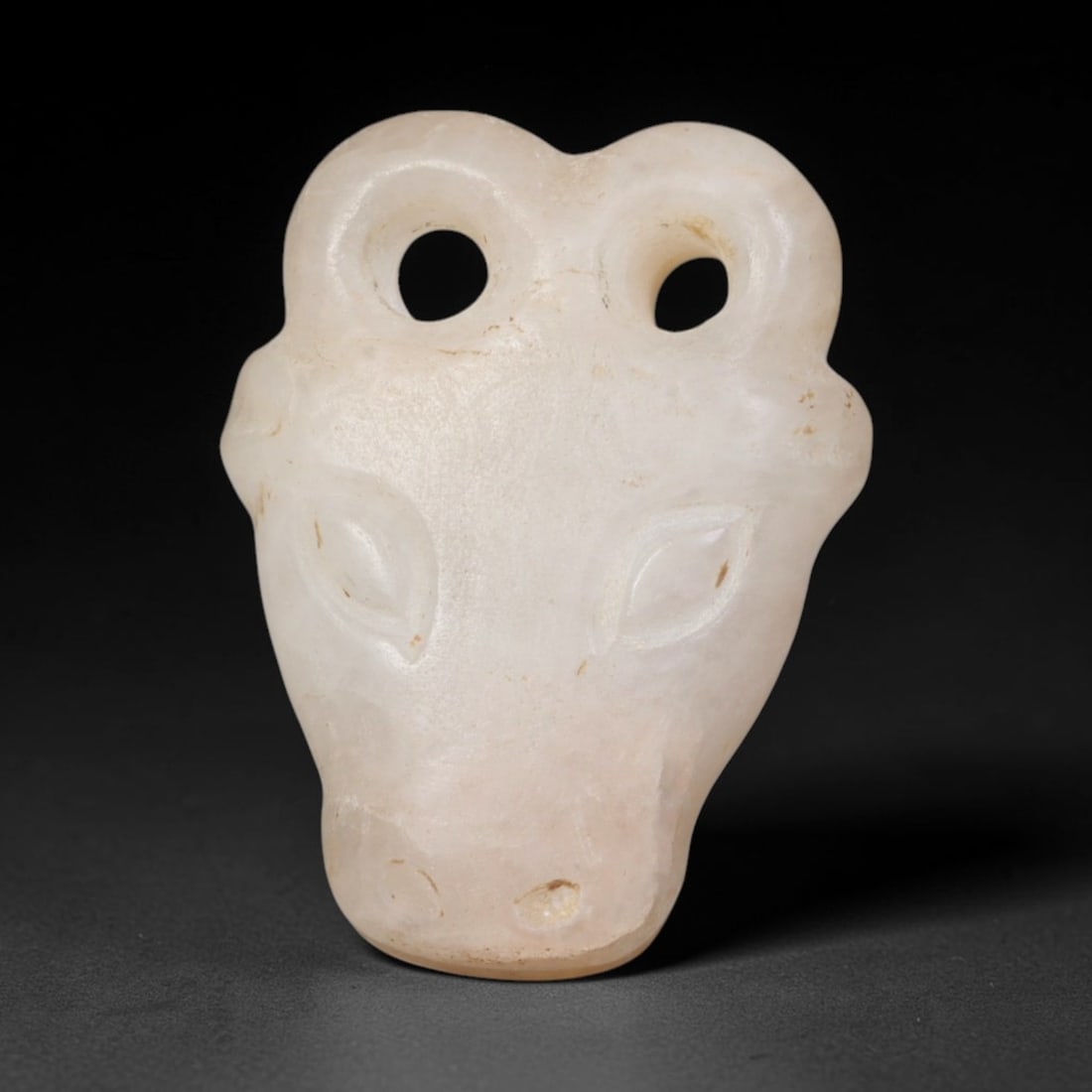 Ancient Bactrian Marble Bull Head Amulet (c.200-200 BCE), 65EQ: Expertly carved from pale creamy white marble originating from ancient Bactria of Central Asia. Rendered as a stylised bull head pendant with two large circular suspension holes integrated into the ho