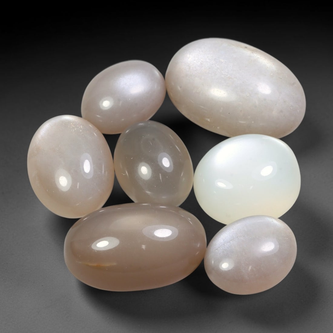 100.25ct Natural Ceylon Moonstone Cabochon Loose Gemstone Parcel Lot, 94EV: This substantial parcel of Ceylon moonstone cabochons showcases soft milky white, warm peach-pink and cool grey-silver tones across smoothly polished oval domed forms. Gentle adularescent sheen drifts