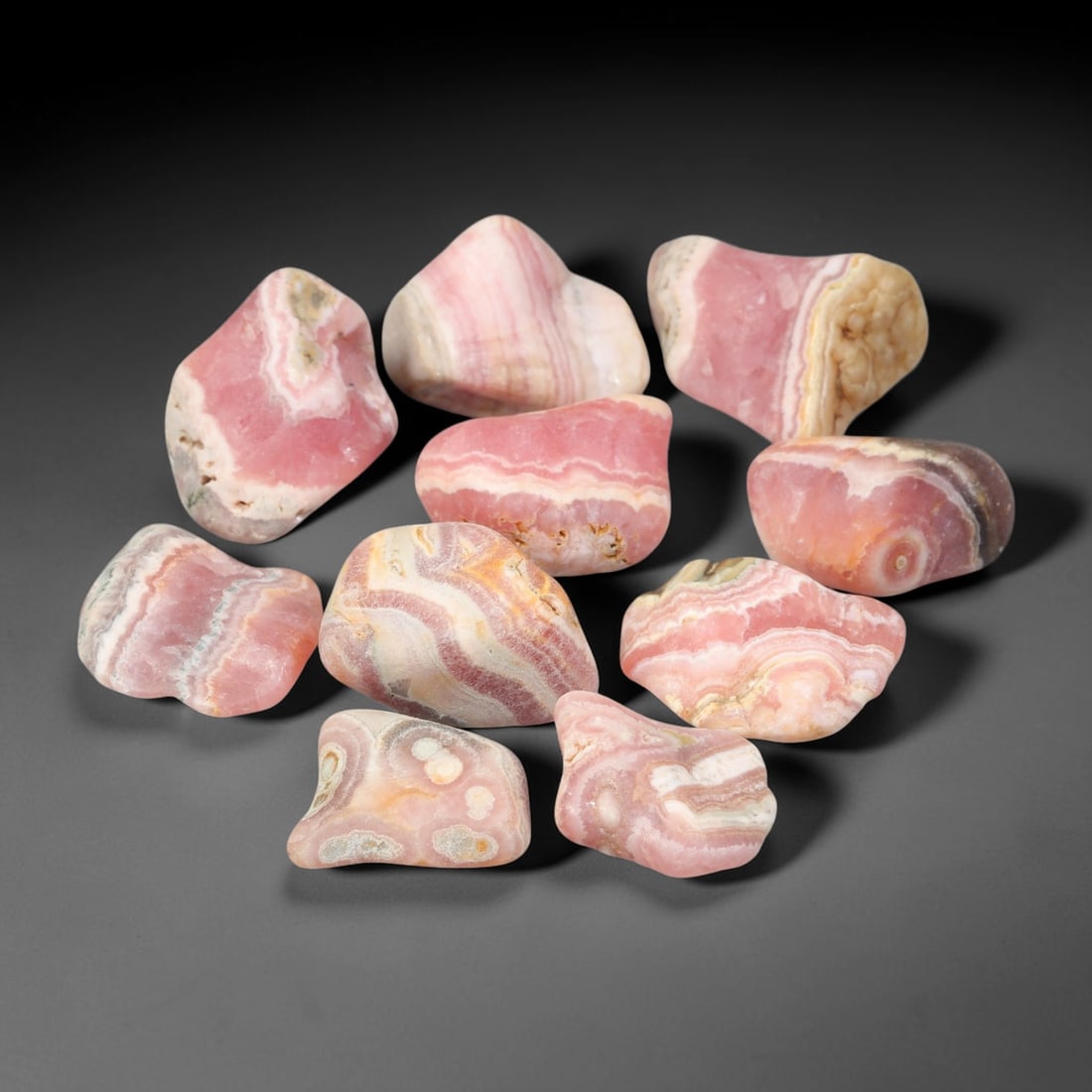 195ct Natural Argentinian Rhodochrosite Tumbled Rough Parcel Lot, 1EW: This beautiful parcel of tumbled rhodochrosite rough showcases striking banded patterning of rich rose-pink, creamy white and subtle earth-toned mineral layers across smooth free-form tumbled surfaces