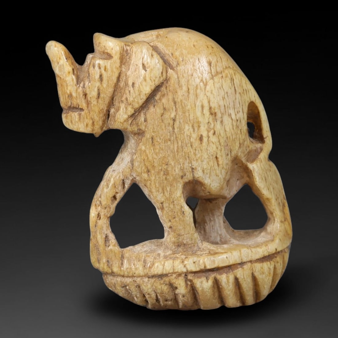 Ancient Indo-Western Asiatic Carved Openwork Bone Elephant Zoomorphic Amulet (800-200 BCE), 25AB: Intricately hand-carved aged bone talisman shaped as a standing elephant with openwork cut-out detailing between its legs, mounted atop a ribbed textured base. Natural warm honeyed aged patina and fin