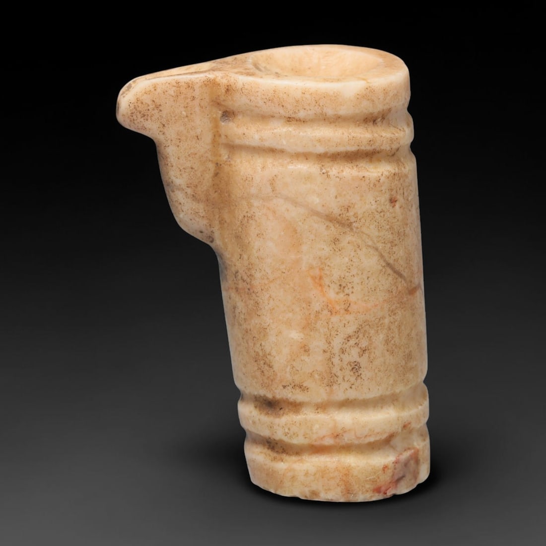 Ancient Near Eastern Calcite Miniature Ritual Vessel (500 BCE - 300 CE), 53EC: This miniature carved calcite ritual pouring vessel originates from the Ancient Near East. The cylindrical body is decorated with incised horizontal raised bands at the base and rim, paired with an in