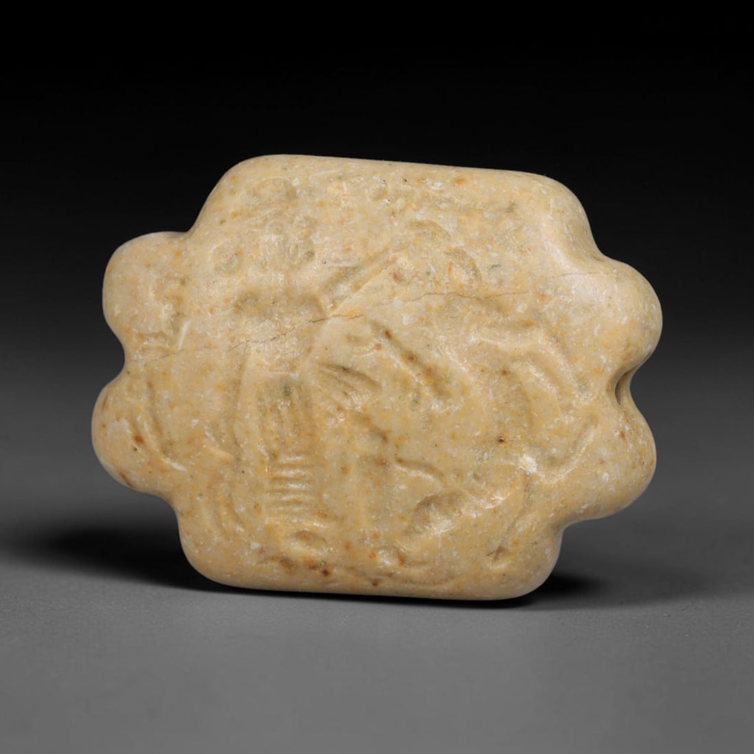 Ancient Sasanian Pale Stone Intaglio Bead (224-651 CE), 87ED: This antique pale beige stone intaglio bead originates from Ancient Sasanian Persian civilisation. The scalloped outline bead features an engraved figural scene across its face. A perforation runs thr