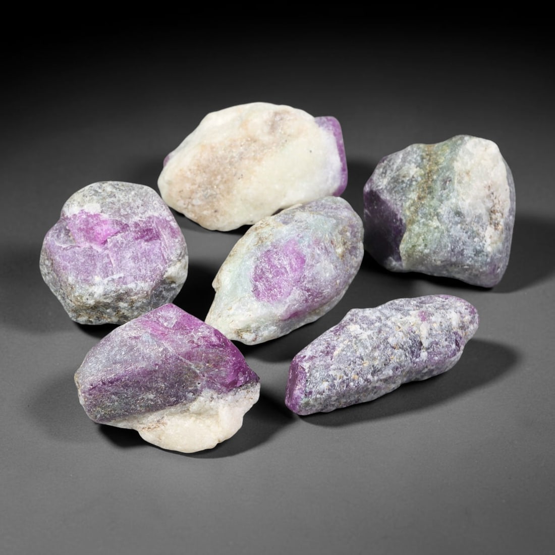 174ct Natural Mauritania Unheated Ruby Rough Parcel Lot, 100EV: This raw parcel of Mauritania ruby rough features vivid magenta-purple crystalline ruby hosted within contrasting pale quartz and mineral matrix. Irregular unpolished specimens display exposed ruby zo