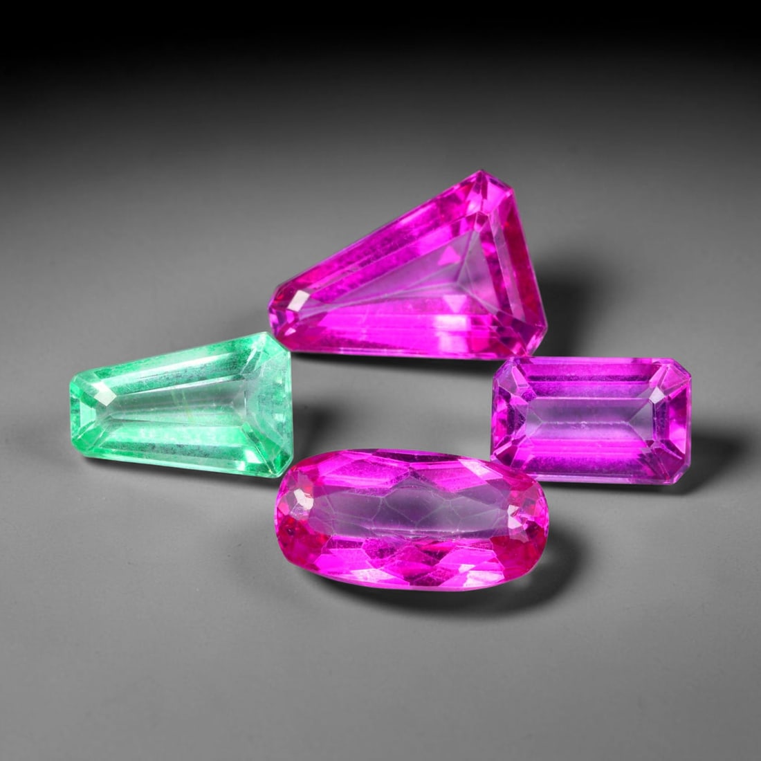 29.01ct Natural Brazilian Color Enhanced Topaz Faceted Parcel Lot, 46EW: This faceted parcel lot showcases mixed geometric cuts of topaz, displaying striking vivid green and intense hot pink colour tones. Each gem features crisp, polished faceting with clean angular silhou
