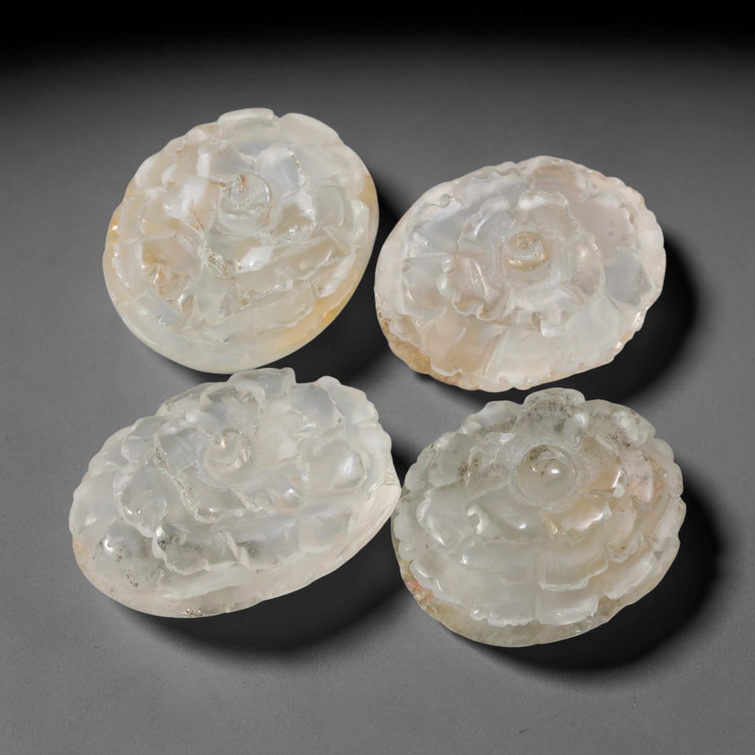 180.05ct Natural Brazilian Carved Phantom Quartz Cabochon Parcel Lot, 52EW: This parcel consists of four oval cabochons carved from natural phantom quartz, featuring finely sculpted multi-layer floral relief motifs across the domed surfaces. The translucent milky-clear quartz