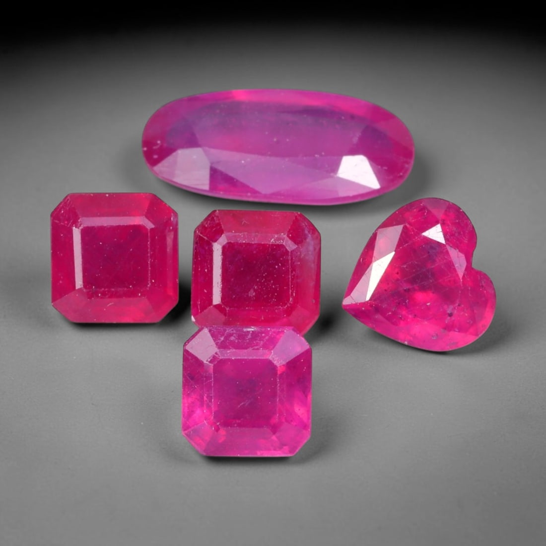 9.39ct Natural Mozambican Ruby Faceted Parcel Lot, 39EW: This faceted gemstone lot features multiple mixed-shape cut rubies displaying rich saturated crimson to vivid pink-red colour tones across oval, heart and square modified faceted forms. Each stone is 