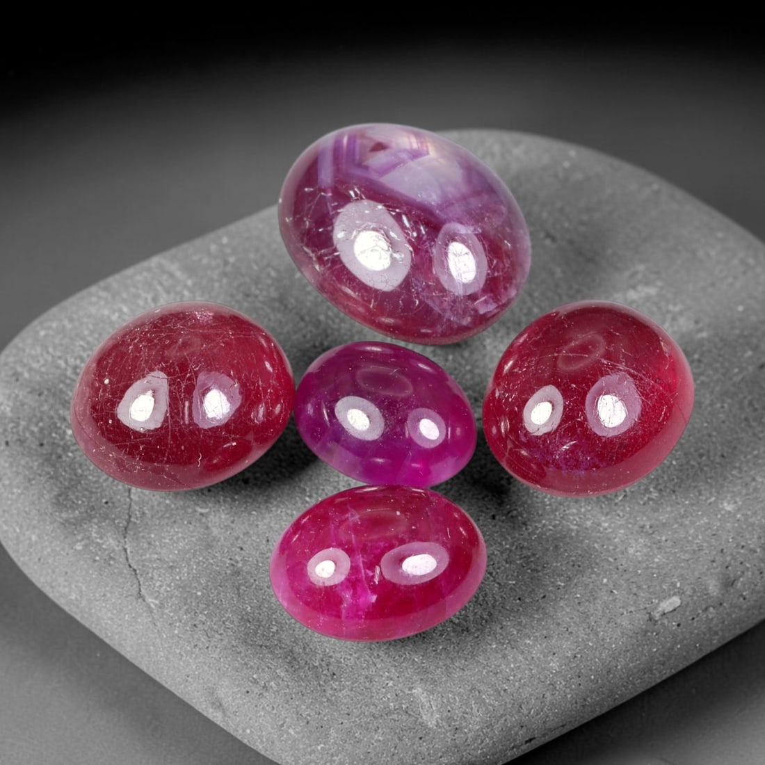 29.61ct Natural Mozambican Ruby Cabochon Parcel Lot, 44EW: This oval cabochon parcel displays rich deep crimson and vivid pink-red ruby tones across domed polished surfaces. Each cabochon features smooth high-gloss finishes, revealing abundant natural silk, f