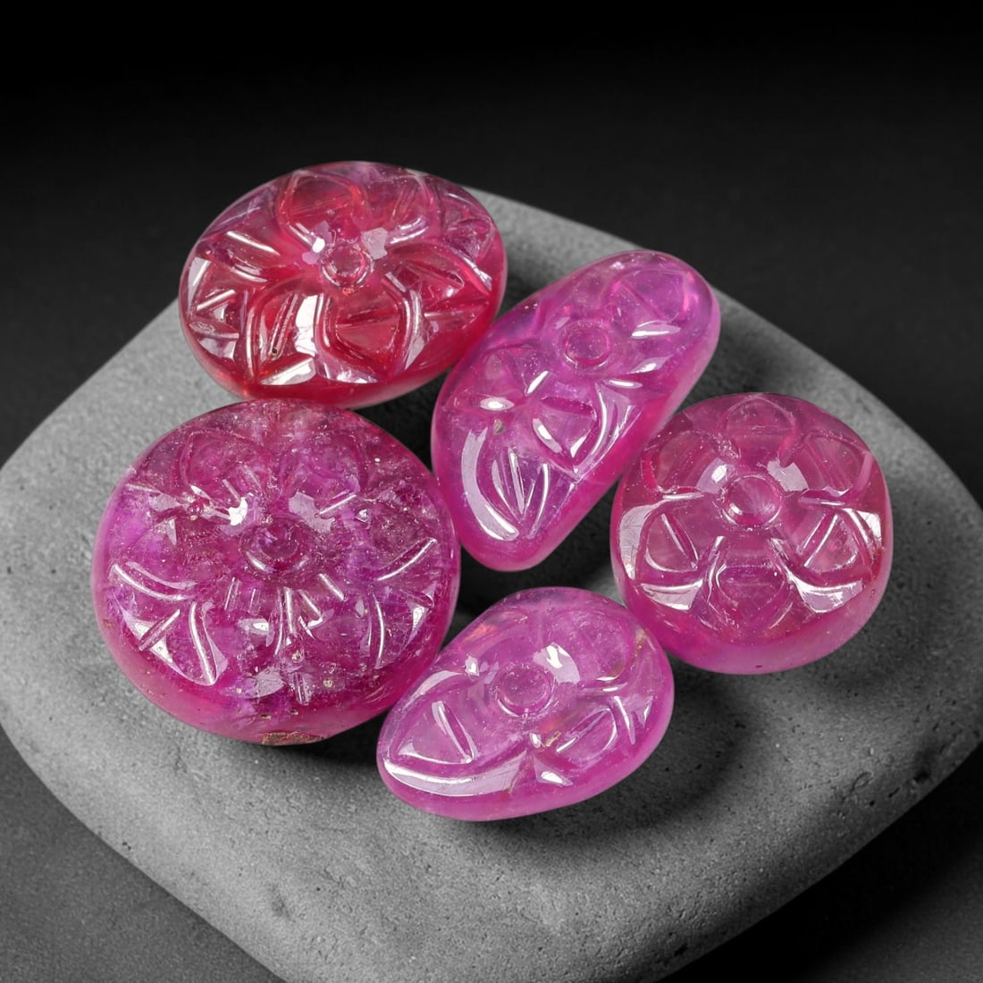 55.32ct Natural Mozambican Carved Ruby Cabochon Parcel Lot, 48EW: This parcel features six ruby cabochons intricately carved with detailed floral relief patterns across domed surfaces. The stones exhibit vibrant magenta-pink to deep ruby-red colour shades, with poli