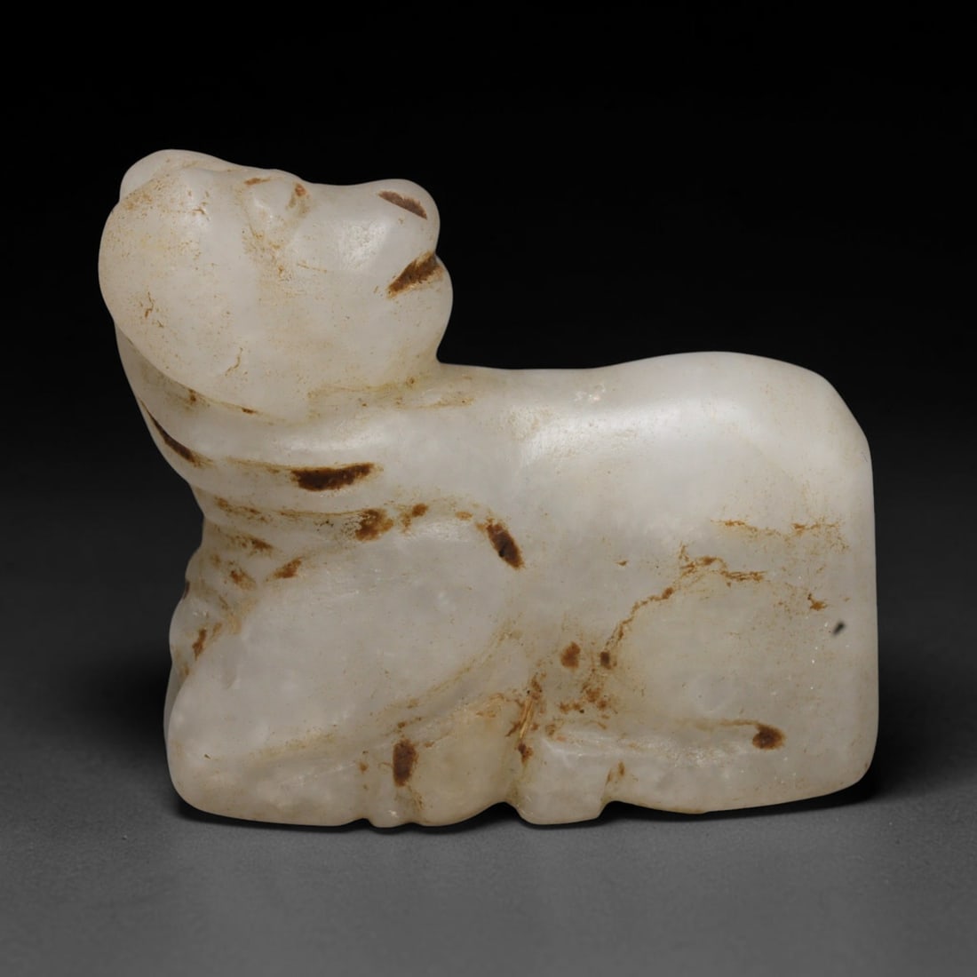 Ancient Near Eastern White Stone Zoomorphic Amulet, 17ED: This antique white stone zoomorphic amulet originates from the Ancient Near East. Carved in recumbent zoomorphic form, the surface displays natural ancient earthy patination. A concealed perforation a