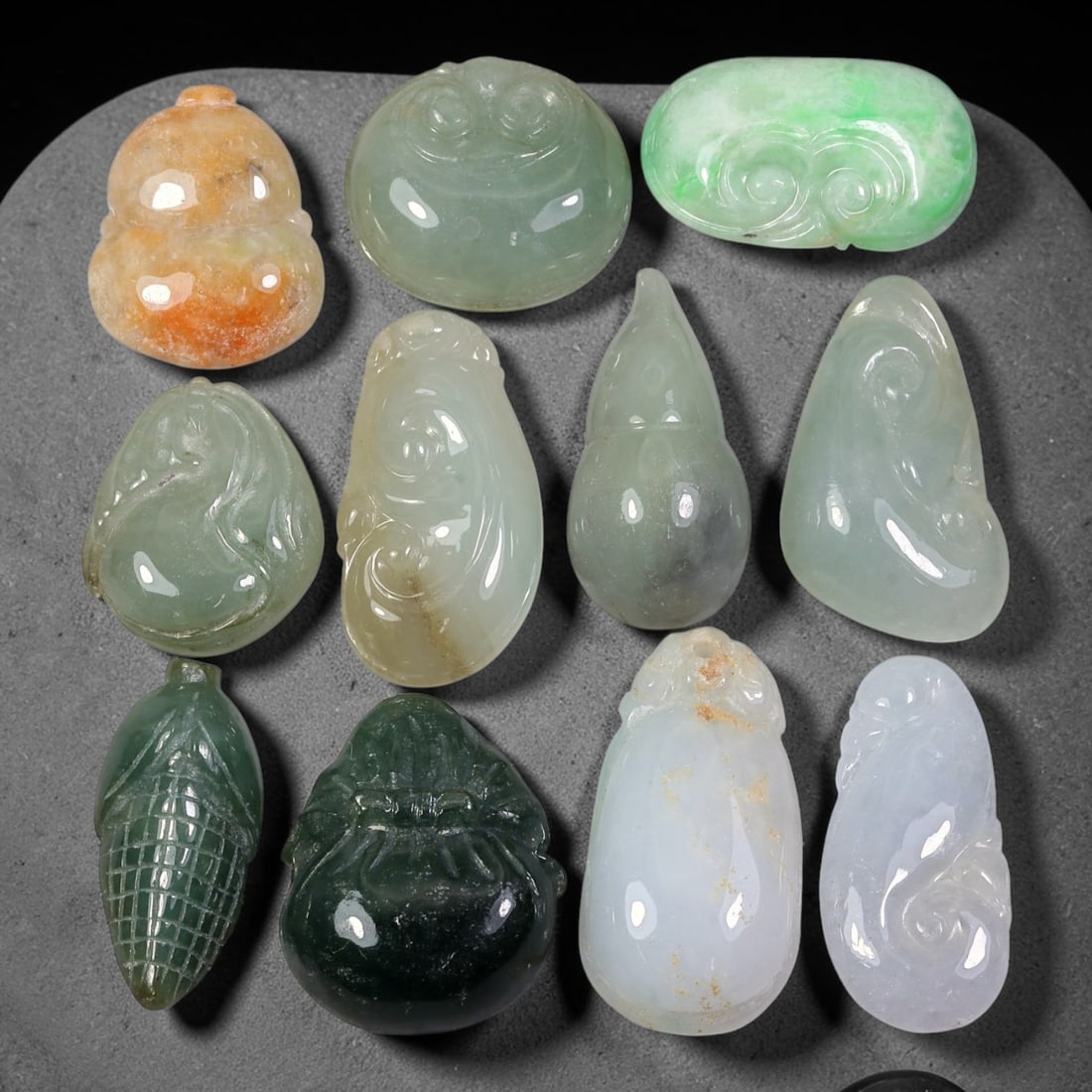 198.62ct Natural Burmese Type A Jadeite Jade Carving Pendant Parcel Lot, 100EX: This parcel lot consists of hand-carved Type A jadeite pendants displaying varied natural colour tones including deep forest green, soft pale green, and warm yellow-gold hues. Each piece finished with