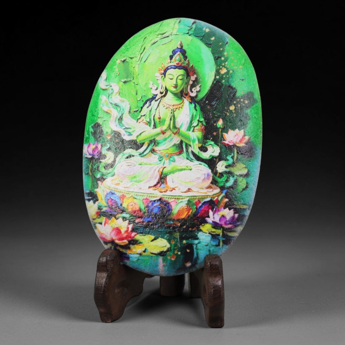 A Tibetan Thangka Style Painted River Stone with a Green Tara, 79BC: Painted on a naturally rounded river stone, the work depicts Green Tara, a female Buddhist deity, in a thangka-style composition. The figure is shown seated in a meditative posture upon a lotus throne