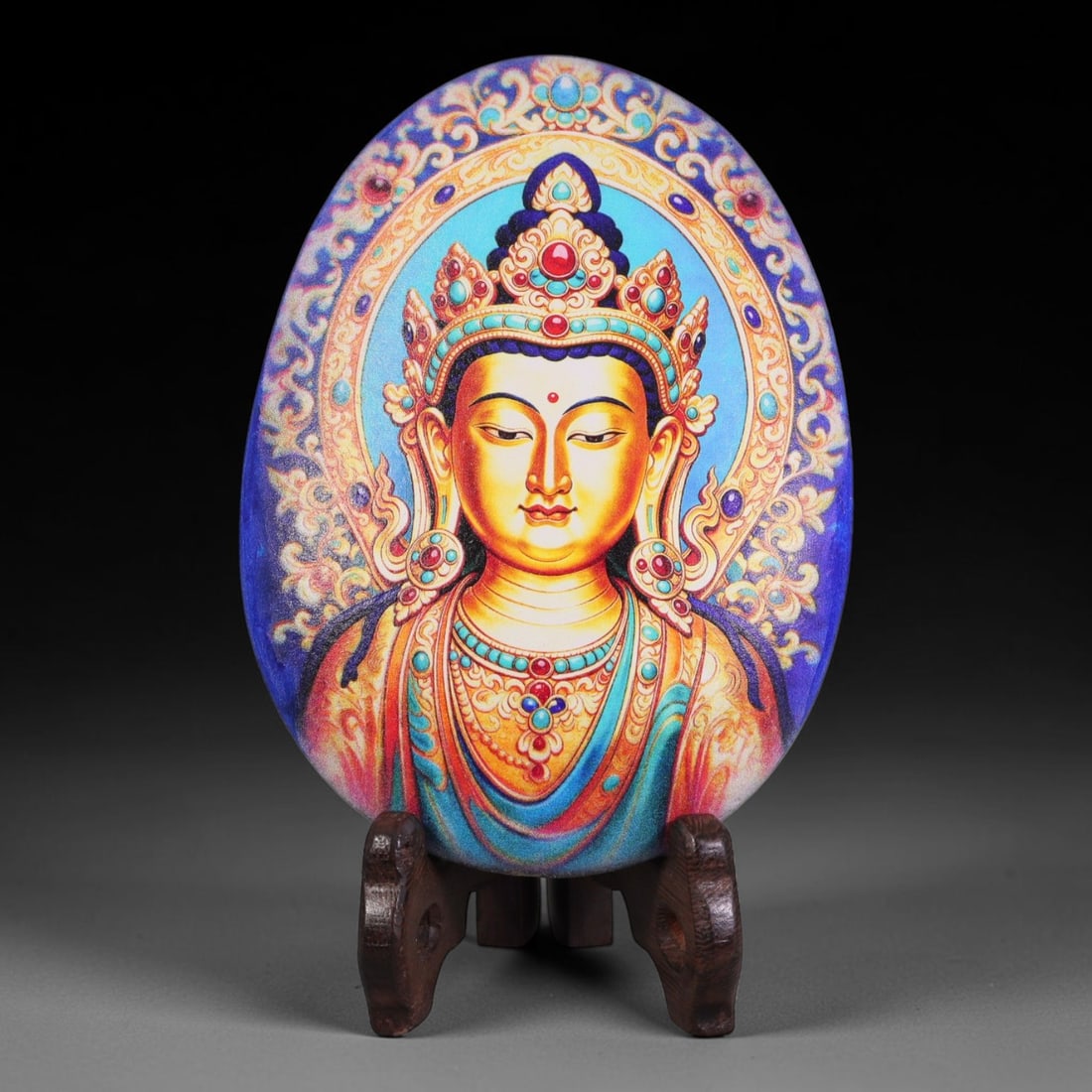 A Tibetan Thangka Style Painted River Stone with a Bodhisattva Figure, 62BC: Painted on a naturally rounded river stone, the work depicts a bodhisattva figure in a thangka-style composition. The figure is shown with a gilded countenance, wearing an ornate jeweled crown and ear