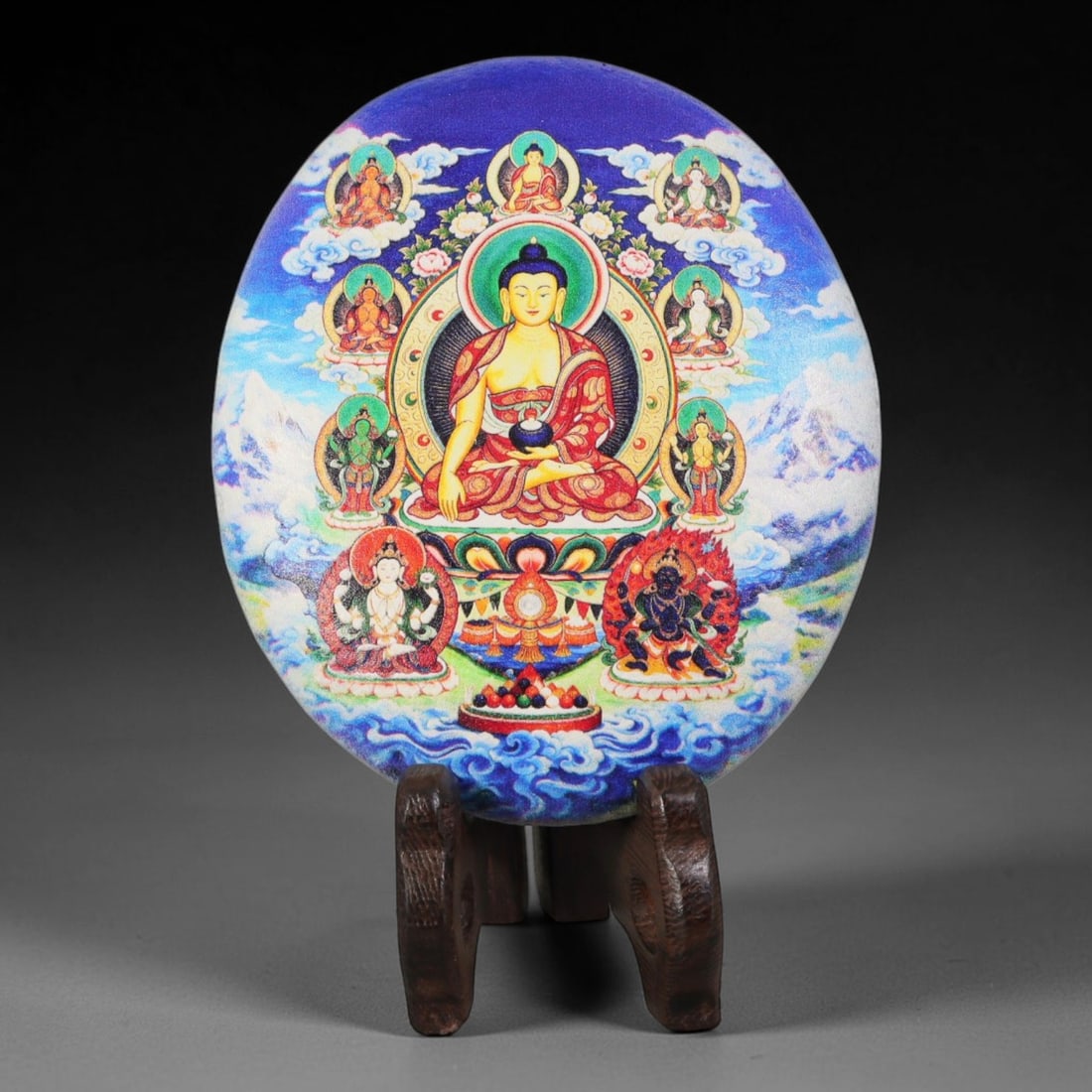 A Tibetan Thangka Style Painted River Stone with a Buddhist Figure, 59BC: Painted on a naturally rounded river stone, the work depicts a seated Buddhist figure in a thangka-style composition. The central figure, likely representing Shakyamuni Buddha, is shown in a meditativ
