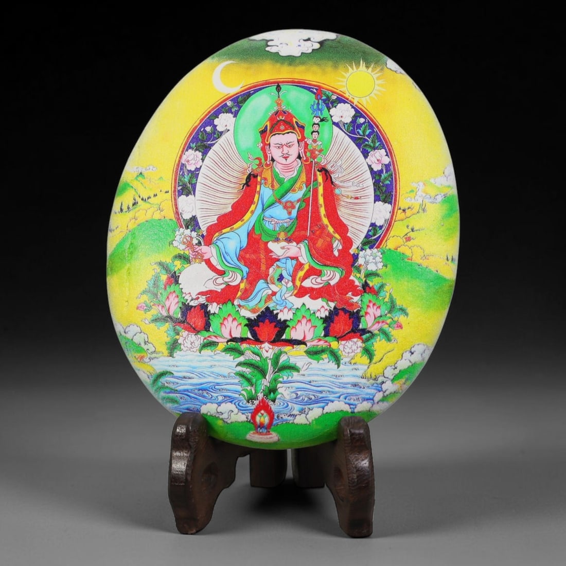 A Tibetan Thangka Style Painted River Stone with a Guru Figure, 68BC: Painted on a naturally rounded river stone, the work depicts a figure of Guru Padmasambhava in a thangka-style composition. The figure is shown seated upon a lotus throne, wearing a red robe with blue