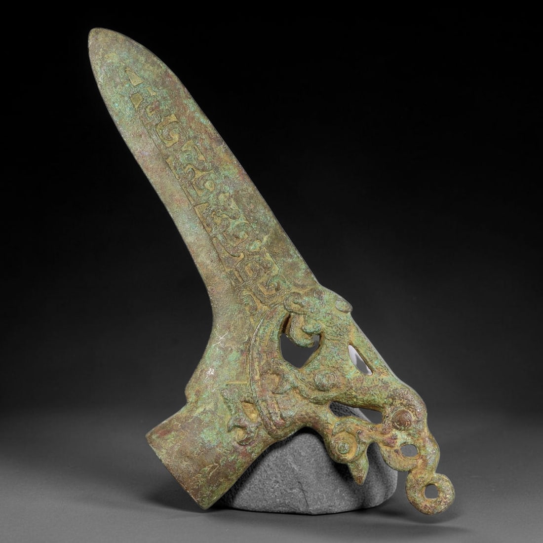 A Chinese Archaic-Style Bronze Ge Dagger-Axe with Openwork Dragon Motif, 98AD: Cast in bronze, this ceremonial ge dagger-axe features a sharp tapering blade decorated along its upper face with continuous archaic scroll and beast-mask relief patterns. The lower haft socket is int
