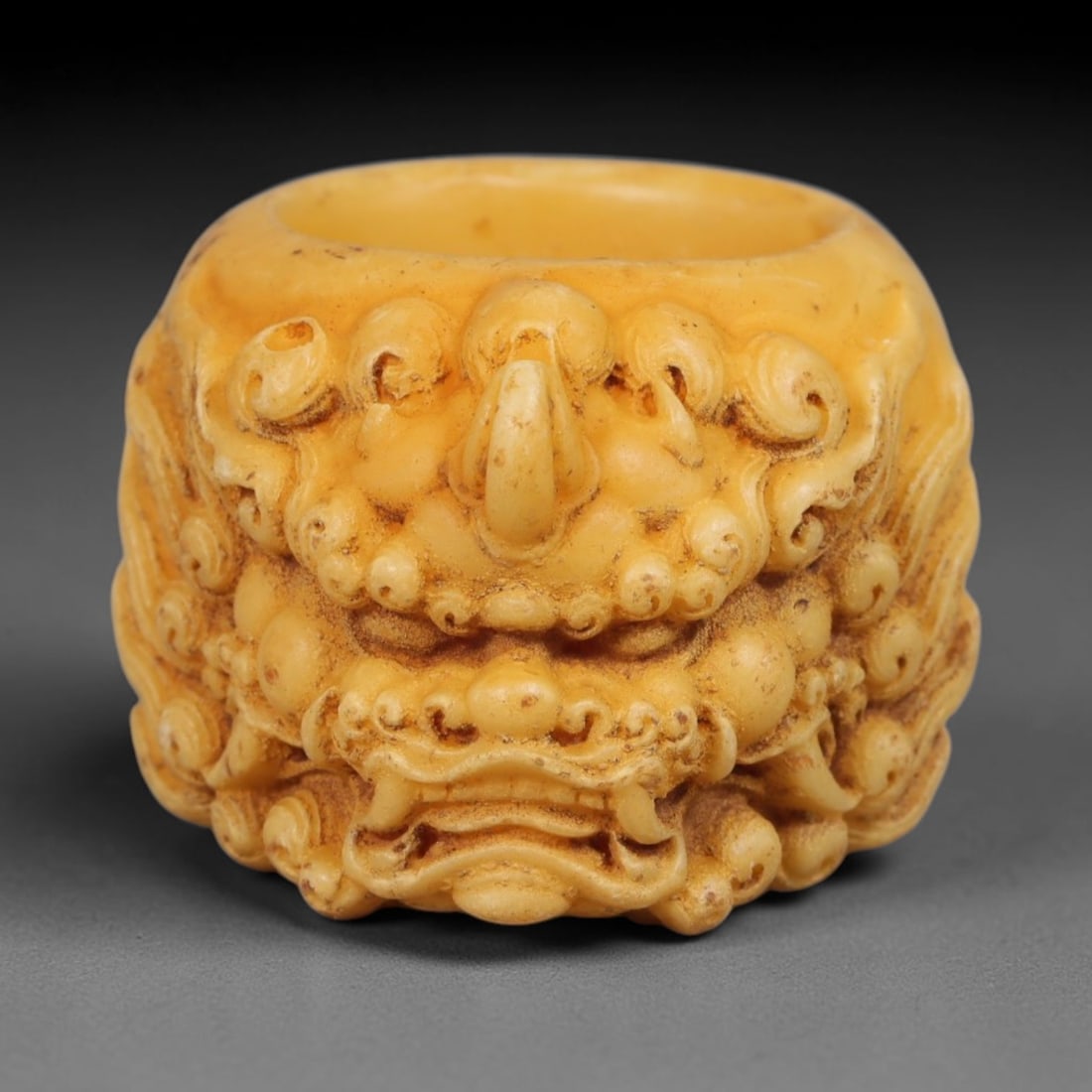 A Chinese Guardian Lion Carved Tagua Nut Thumb Ring, 82BC: Carved from tagua nut, this solid thumb ring features deeply sculpted guardian lion motif upon its outer surface. Detailed curled manes, rounded facial features and ornate scrollwork define the mythic