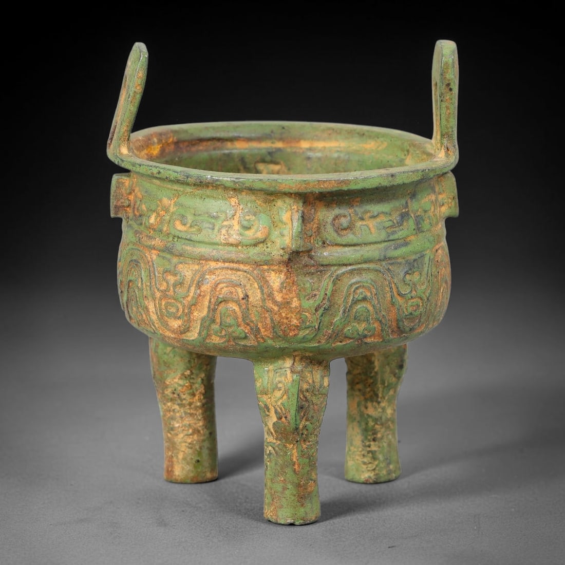 A Chinese Archaic-Style Bronze Tripod Ding Vessel, 72AD: Cast in bronze, this miniature tripod ding vessel features two upright rectangular loop handles rising from the broad rim. The rounded bulbous body is decorated with two bands of relief archaic beast 
