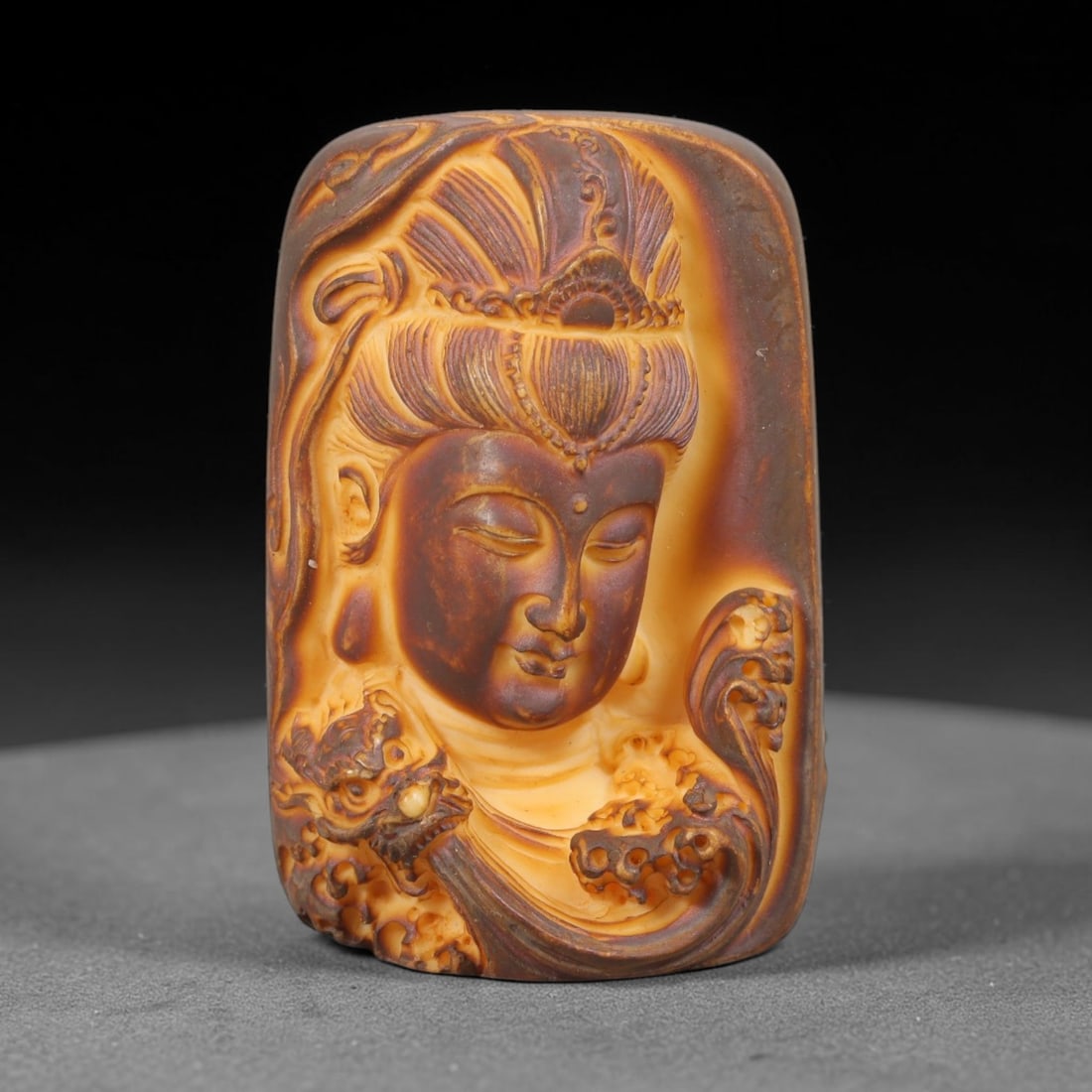 A Chinese Guanyin Deity Carved Tagua Nut Pendant Amulet, 2AD: Carved from tagua nut, this rectangular tablet-form amulet is executed in high relief. The central field depicts the head and upper torso of a Bodhisattva, identifiable as Guanyin, with downcast eyes,
