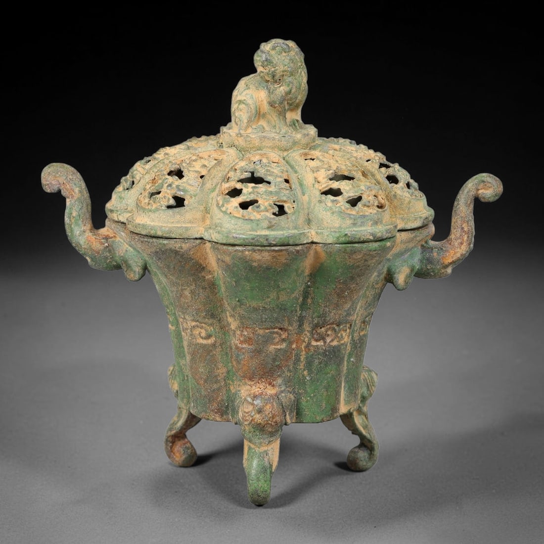 A Chinese Bronze Lion-Finial Tripod Censer, 66AD: Cast in bronze, this tripod censer features lobed body moulded with subtle archaic scroll motifs across its exterior. The openwork pierced lid is crowned with a seated guardian lion finial, allowing i