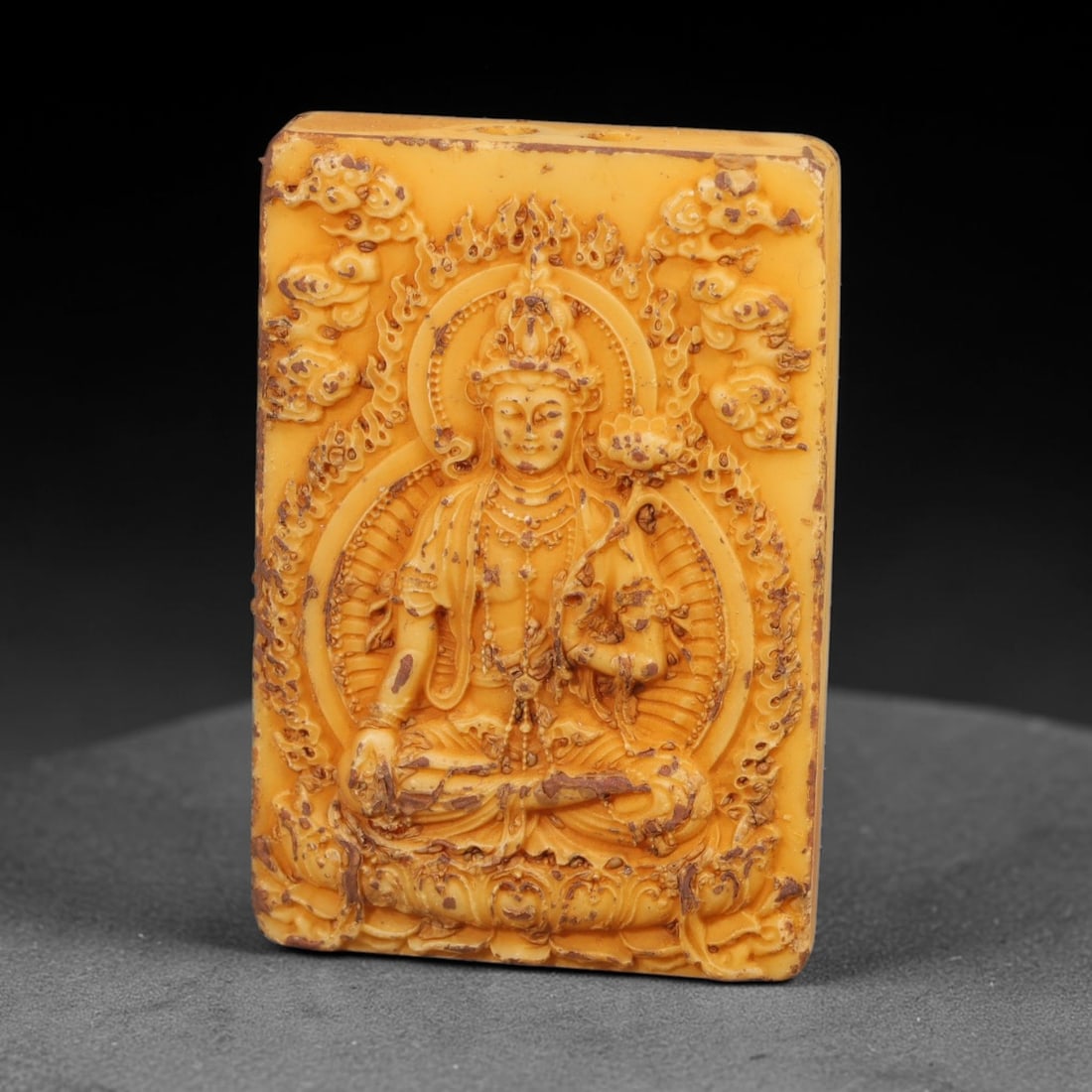 A Chinese Guanyin Deity Carved Tagua Nut Pendant Amulet, 88BC: Carved from tagua nut, this rectangular tablet-form amulet is rendered in high relief. The Guanyin figure is seated in lotus posture atop an ornate lotus base, displaying varada mudra with the right h