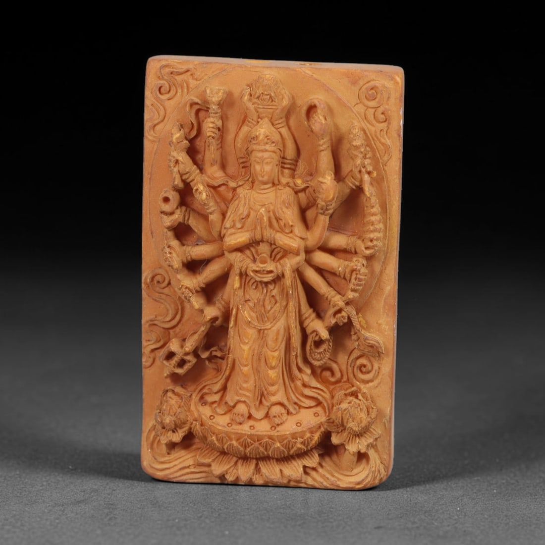 A Chinese Multi-Armed Guanyin Deity Carved Tagua Nut Pendant Amulet, 83BC: Carved from tagua nut, this rectangular tablet-form amulet is rendered in high relief. The multi-armed Guanyin stands upon a detailed lotus pedestal, central hands joined in anjali mudra at the chest,